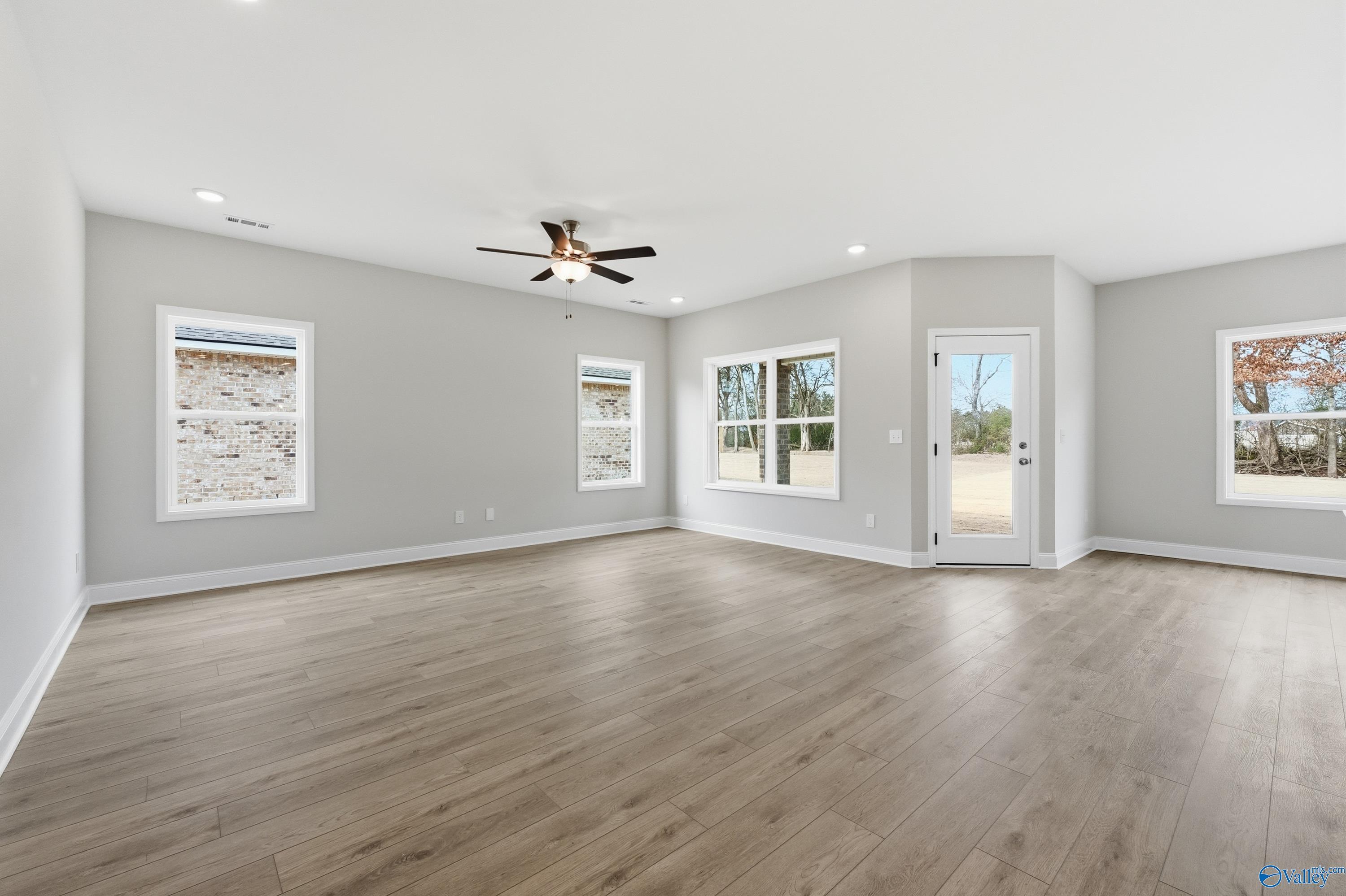 Bright living room with hardwood floors, ceiling fan, and large windows in The Franklin 3-bedroom home by Davidson Homes, Meridianville, Alabama