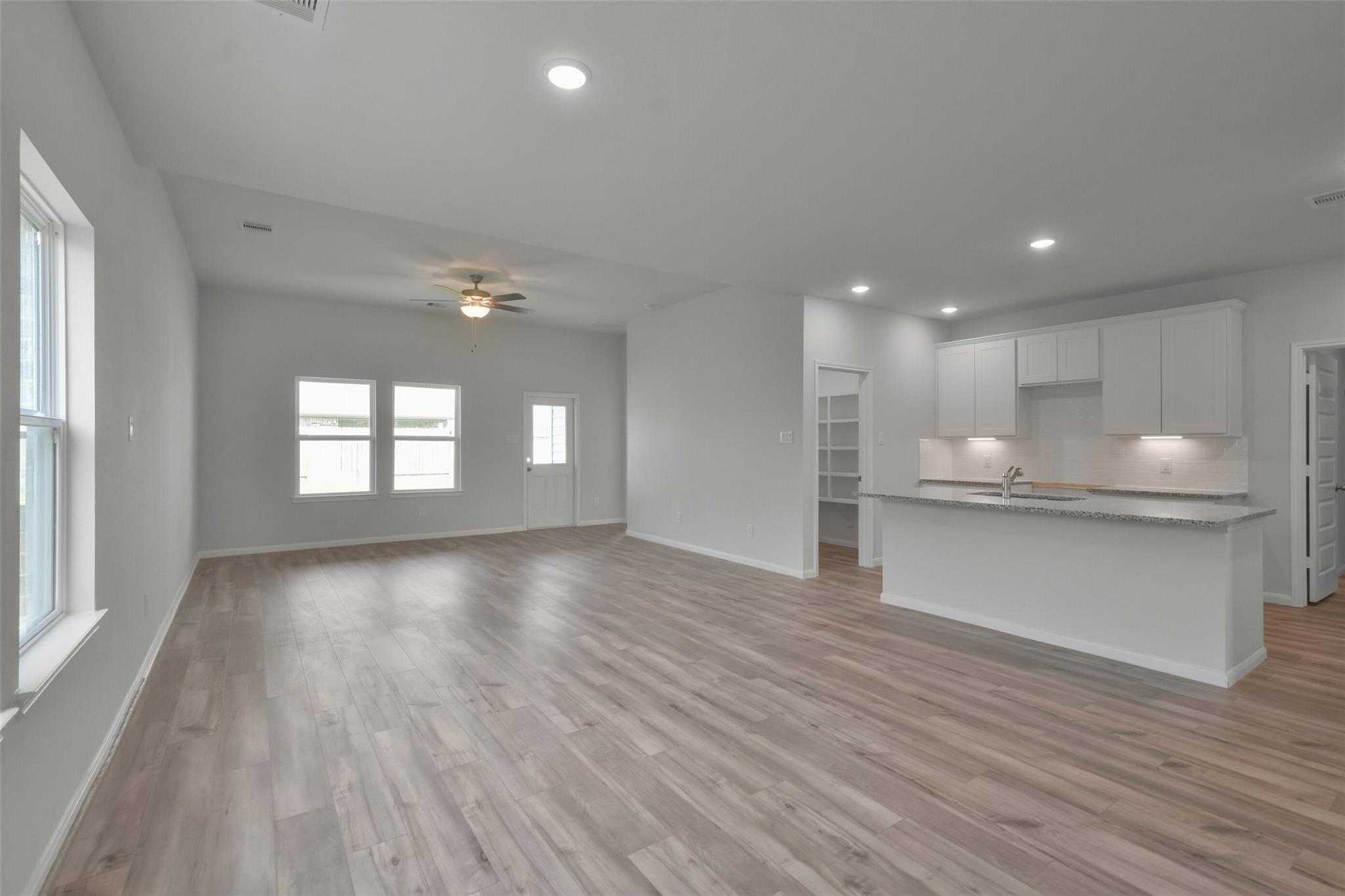 Open-concept living room and kitchen with white cabinets, island sink, ceiling fan, and large windows in Davidson Homes The Tierra A, Dayton Texas