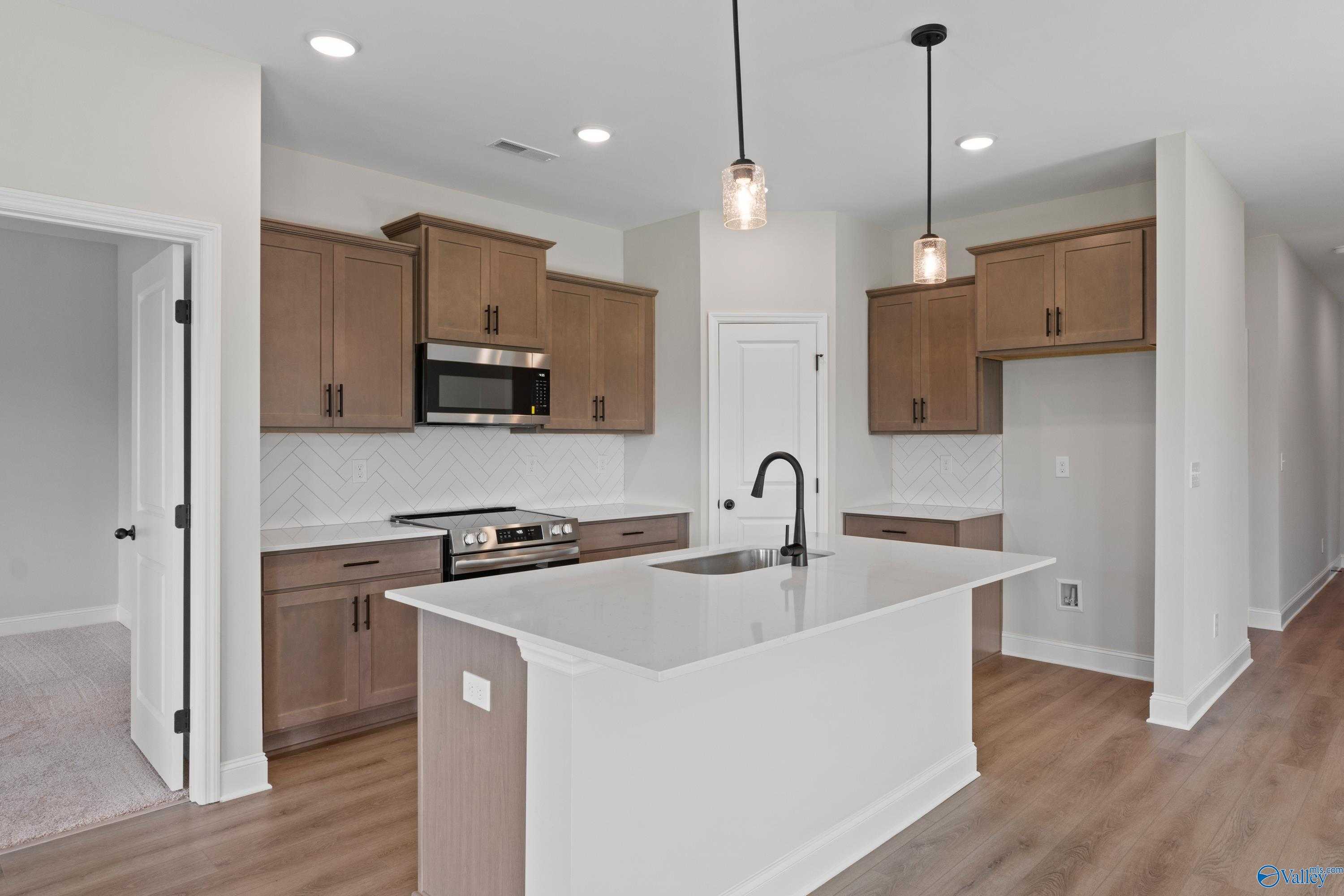Modern kitchen with white quartz island, stainless appliances, subway tile backsplash, and shaker cabinets in Davidson Homes Franklin C, Hazel Green AL
