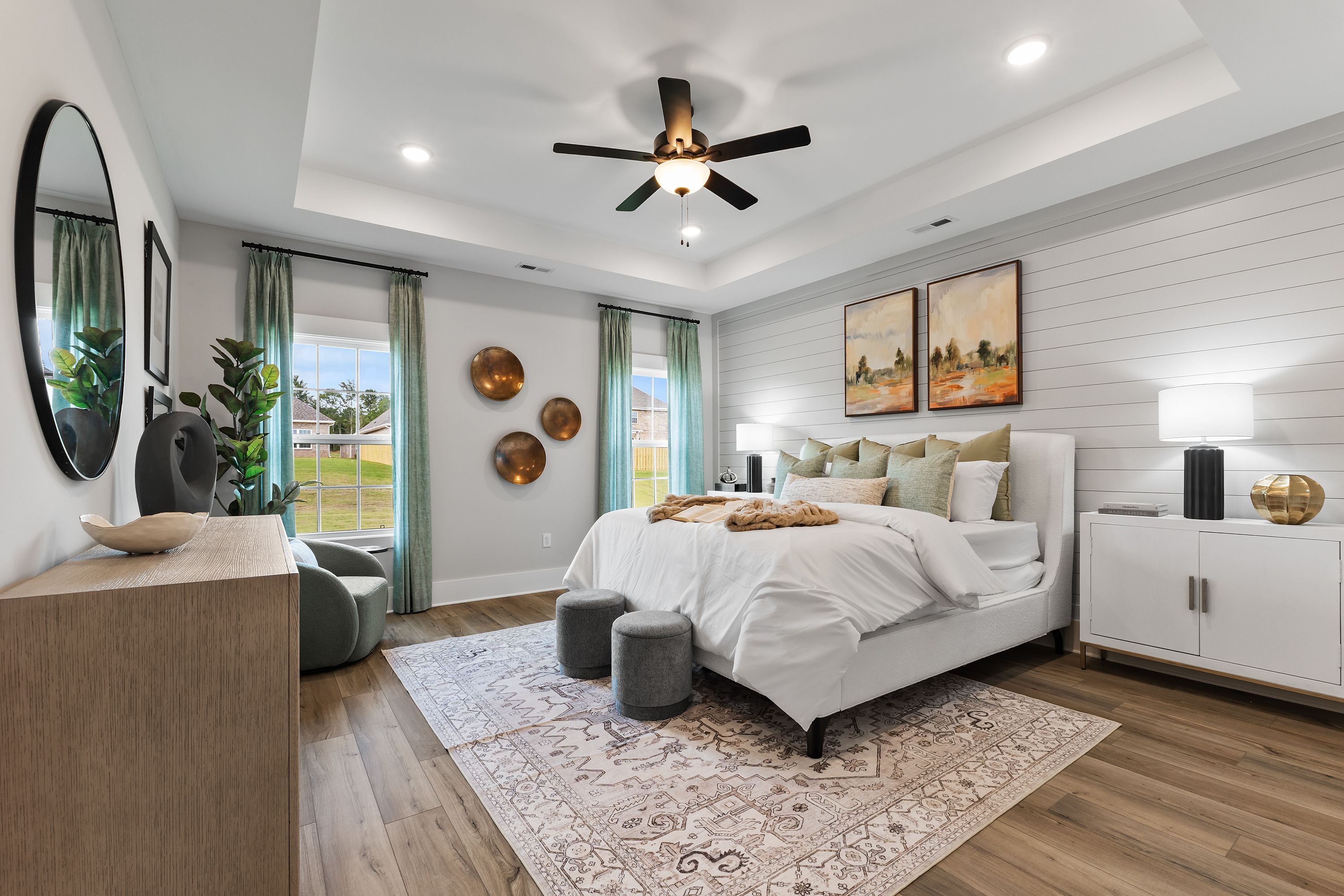 Spacious primary bedroom at River Road Estates in Decatur, Alabama with king bed, shiplap wall, hardwood floors, and ceiling fan