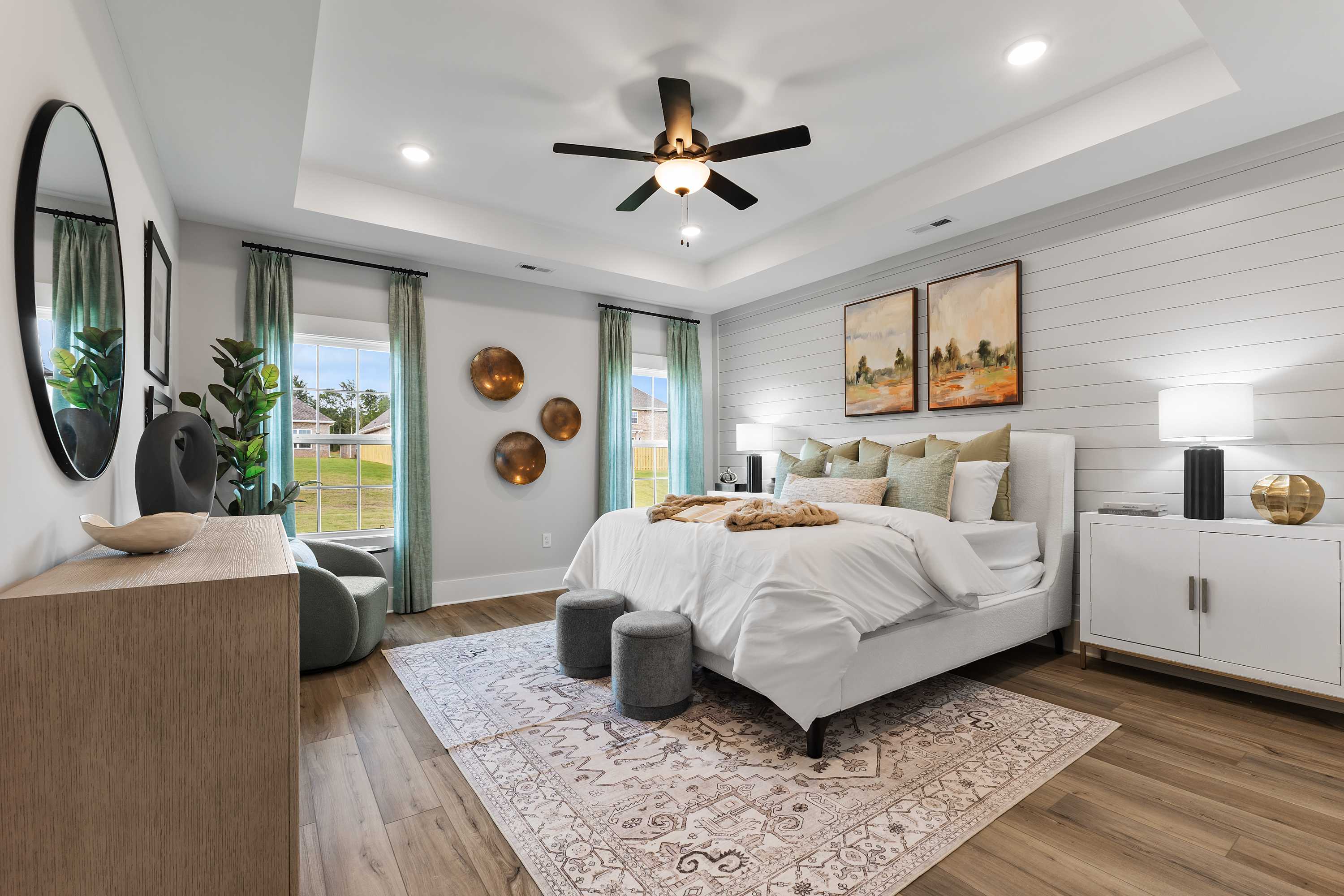 Spacious primary bedroom at River Road Estates in Decatur, Alabama with king bed, shiplap wall, hardwood floors, and ceiling fan