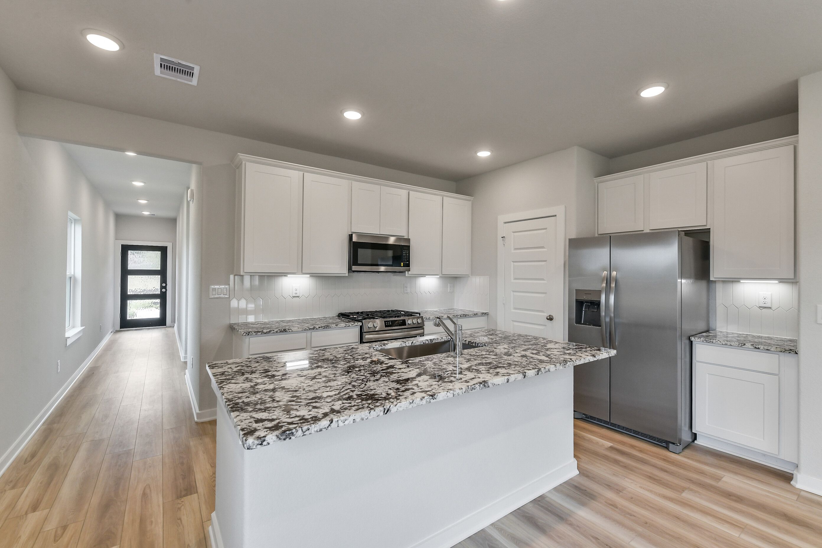 Open-concept kitchen with white shaker cabinets, speckled granite island, stainless appliances in Davidson Homes The Colorado G, Magnolia TX