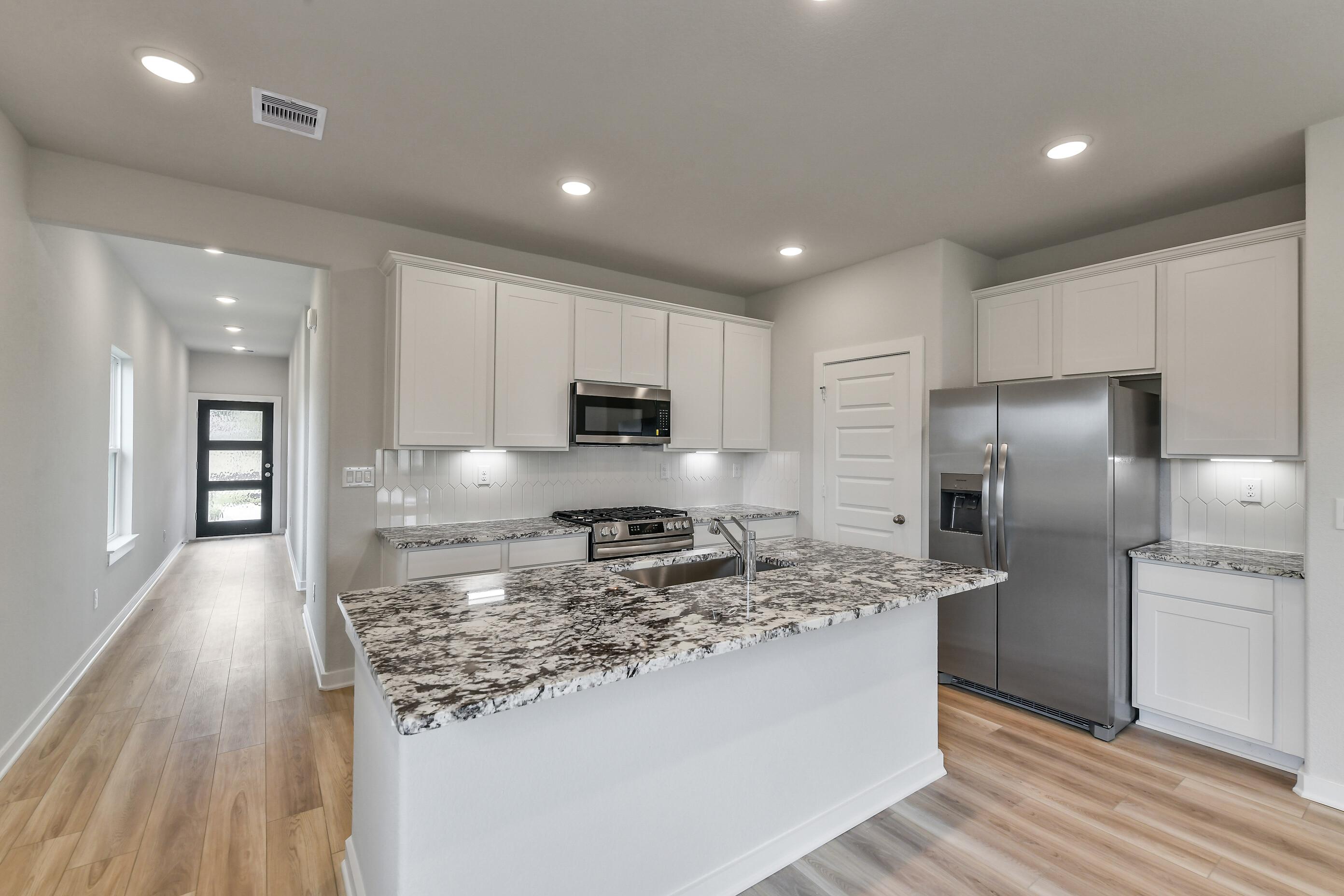 Open-concept kitchen with white shaker cabinets, speckled granite island, stainless appliances in Davidson Homes The Colorado G, Magnolia TX