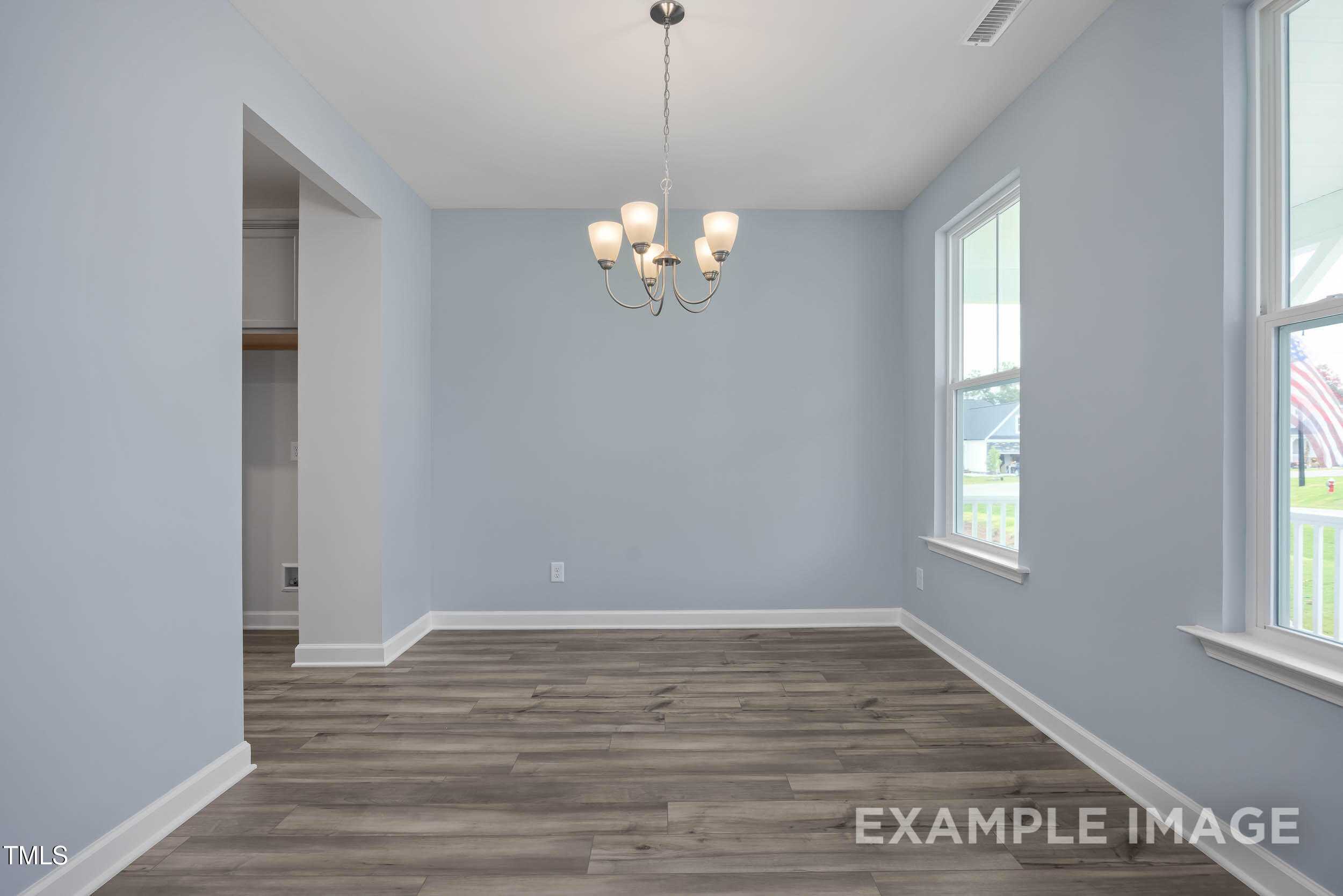 Elegant dining room with light blue walls, hardwood floors, chandelier, and large windows in The Willow E 4-bedroom home, Angier, NC