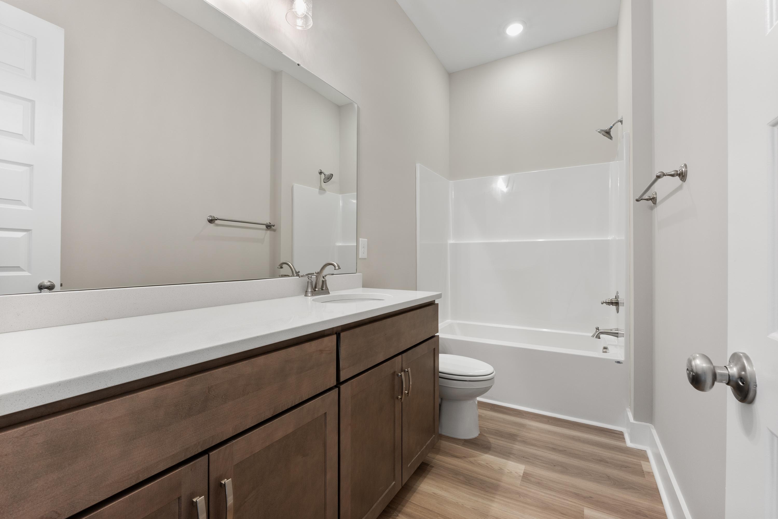 Modern master bathroom in The Oxford by Evermore Homes featuring double quartz vanity, soaking tub, walk-in shower, and hardwood floors