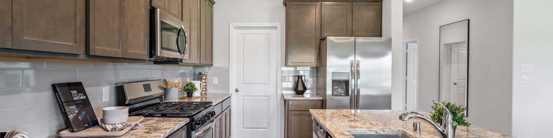 Spacious modern kitchen at Windmill Estates in Magnolia Texas with taupe cabinets, granite island, stainless steel appliances, hardwood floors