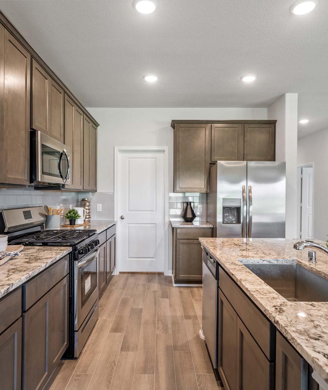 Spacious modern kitchen at Windmill Estates in Magnolia Texas with taupe cabinets, granite island, stainless steel appliances, hardwood floors