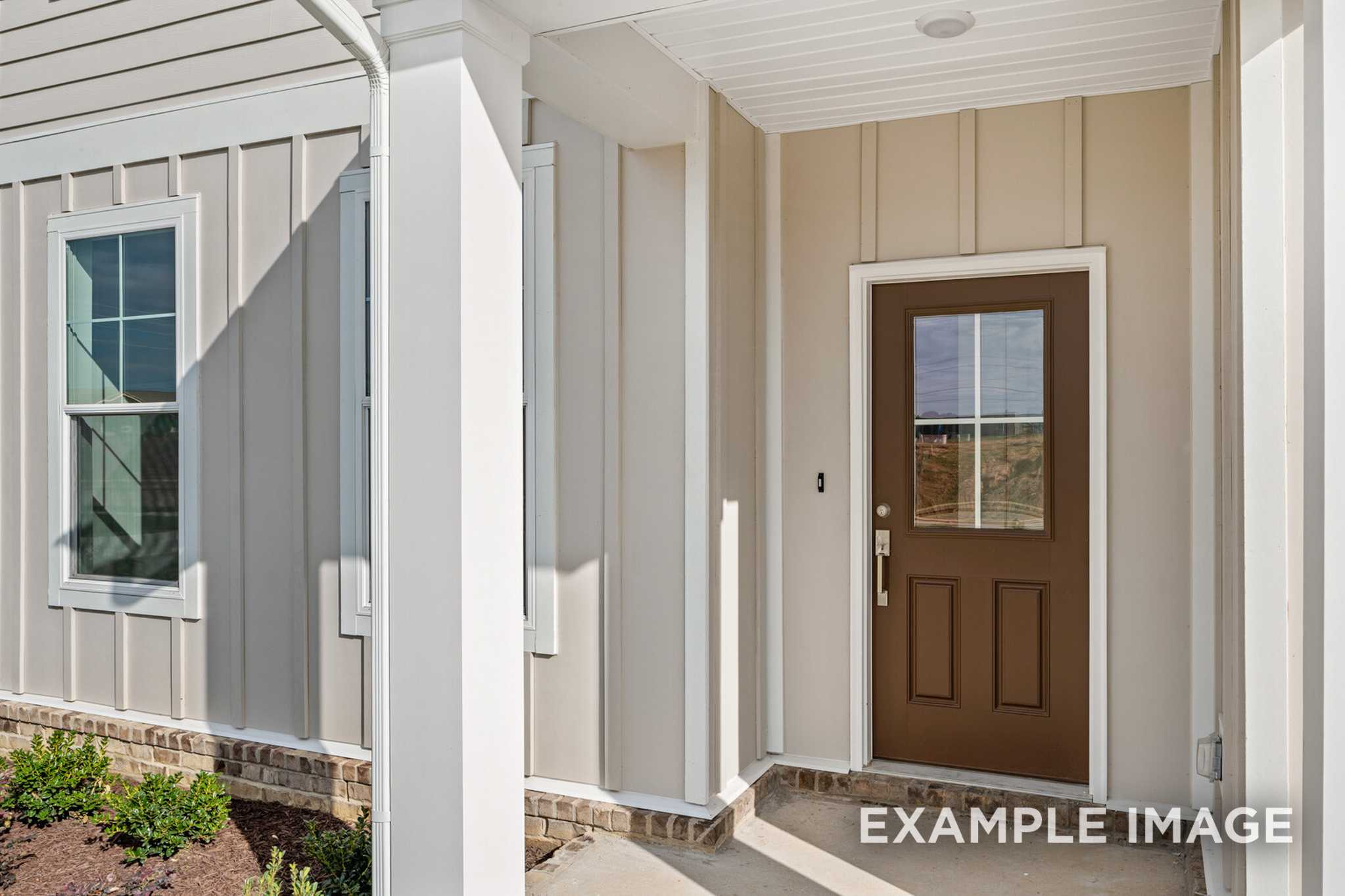 Front porch entry of The Murray A Davidson Homes design with beige siding, white trim, paneled wood door, and brick base in White House TN