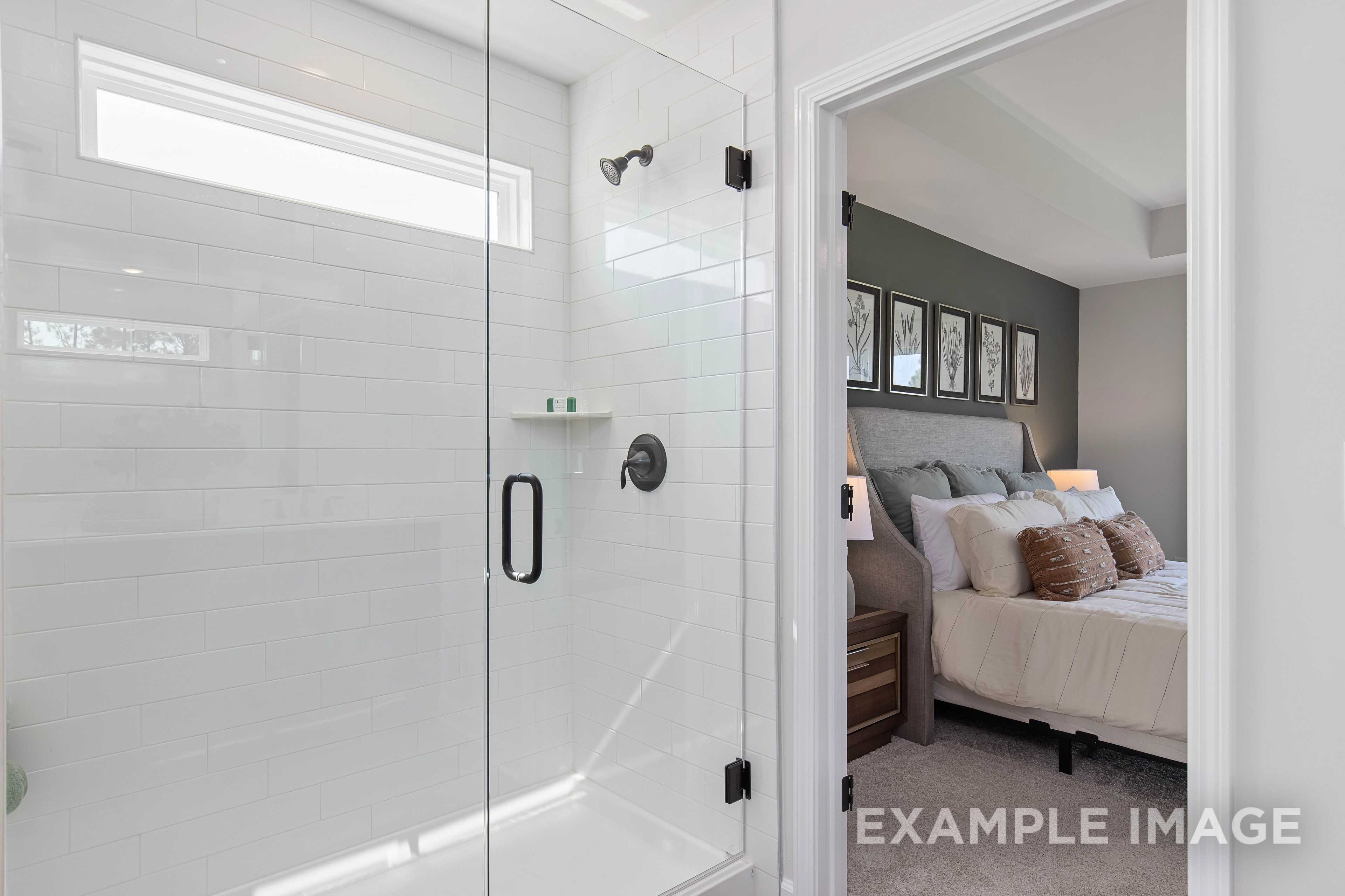 Frameless glass shower in The Willow B master bath with white subway tiles, open to upper floor bedroom with king bed