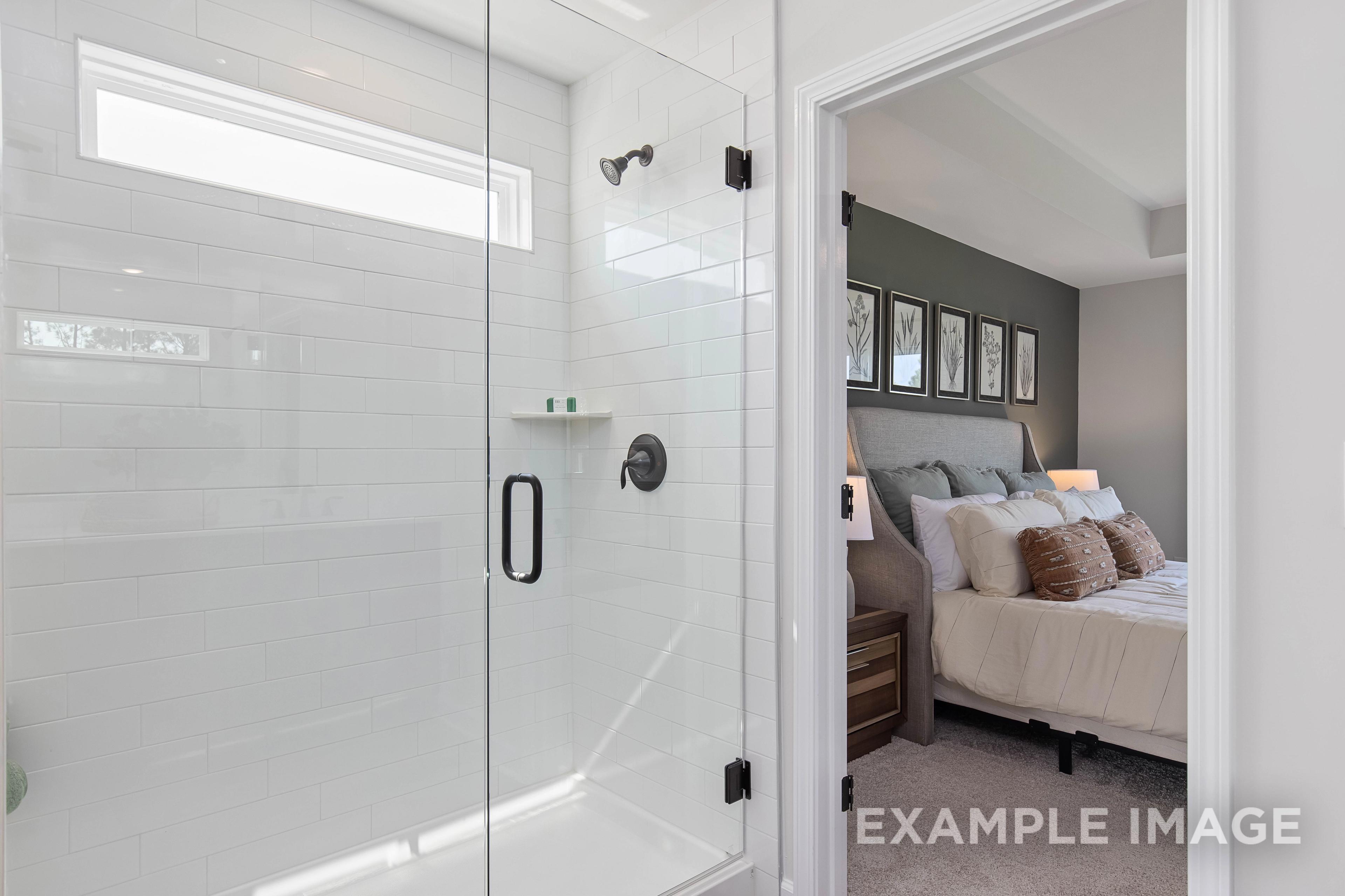 Frameless glass shower in The Willow B master bath with white subway tiles, open to upper floor bedroom with king bed