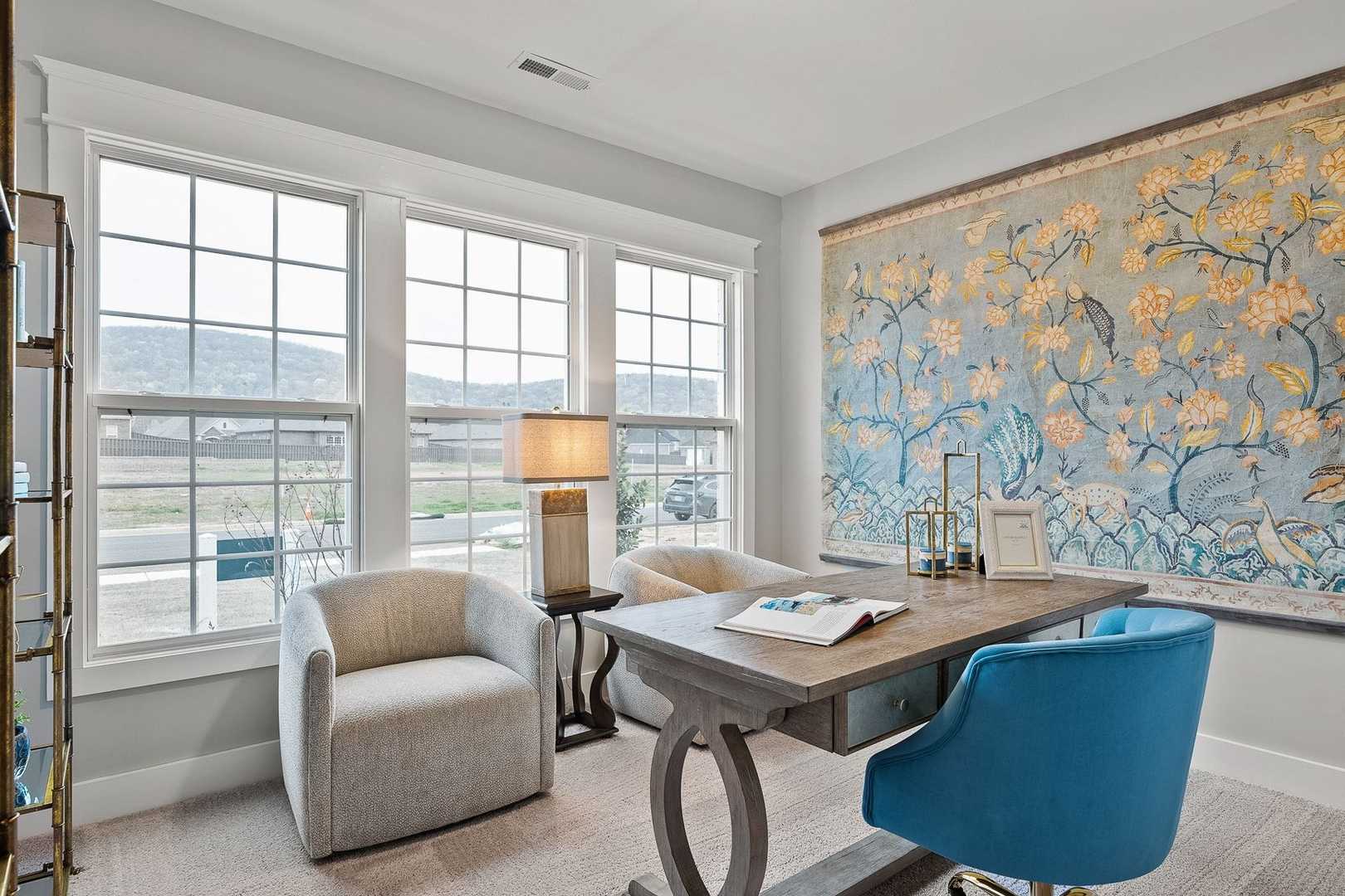 Spacious home office in The Oxford by Evermore Homes with scenic mountain views, wooden desk, armchairs, and floral wall tapestry