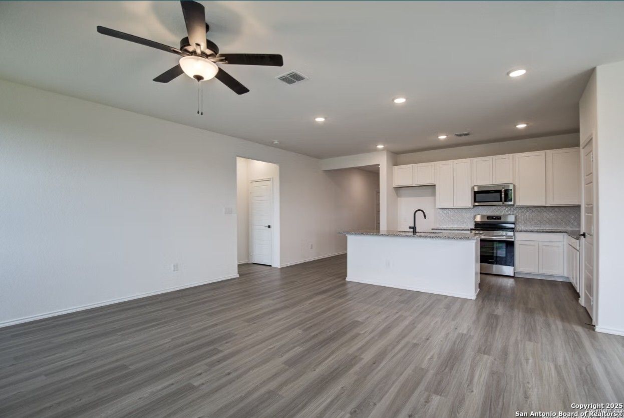 Open-concept kitchen and living area with white cabinets, stainless steel appliances, island sink, and ceiling fan in The Daphne H, Seguin, Texas