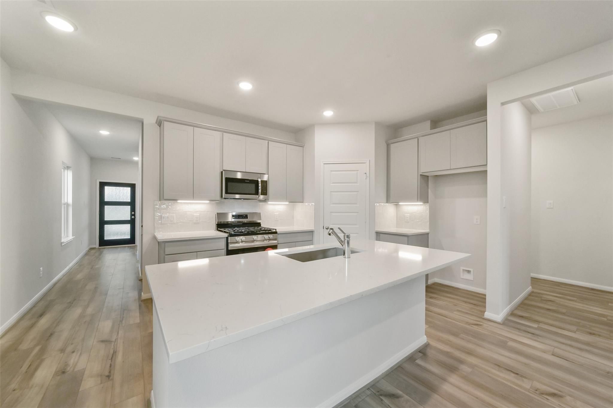Modern white shaker kitchen with quartz island, gas range, and stainless appliances in Davidson Homes San Marcos E, Beasley, Texas