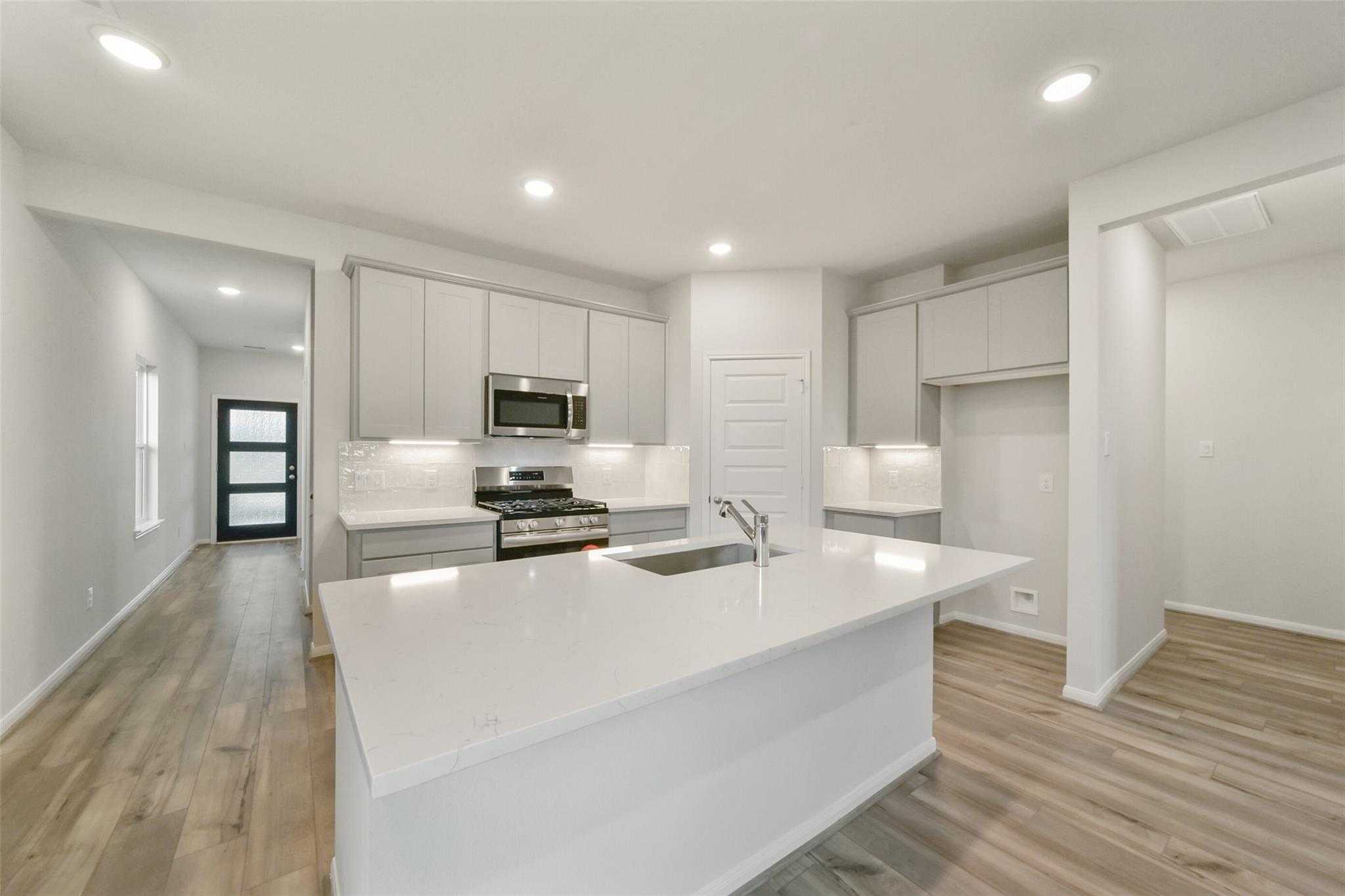 Modern white shaker kitchen with quartz island, gas range, and stainless appliances in Davidson Homes San Marcos E, Beasley, Texas