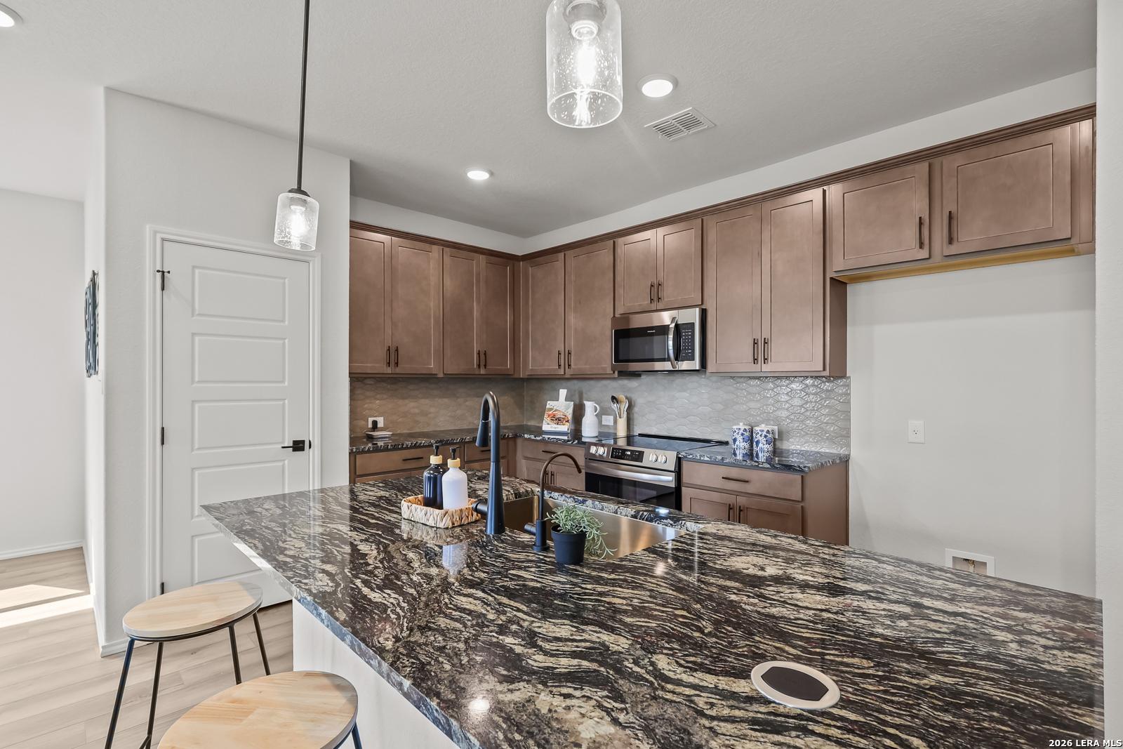 Modern kitchen featuring granite island, shaker cabinets, stainless appliances in The Daphne H 3-bedroom home, Seguin, Texas