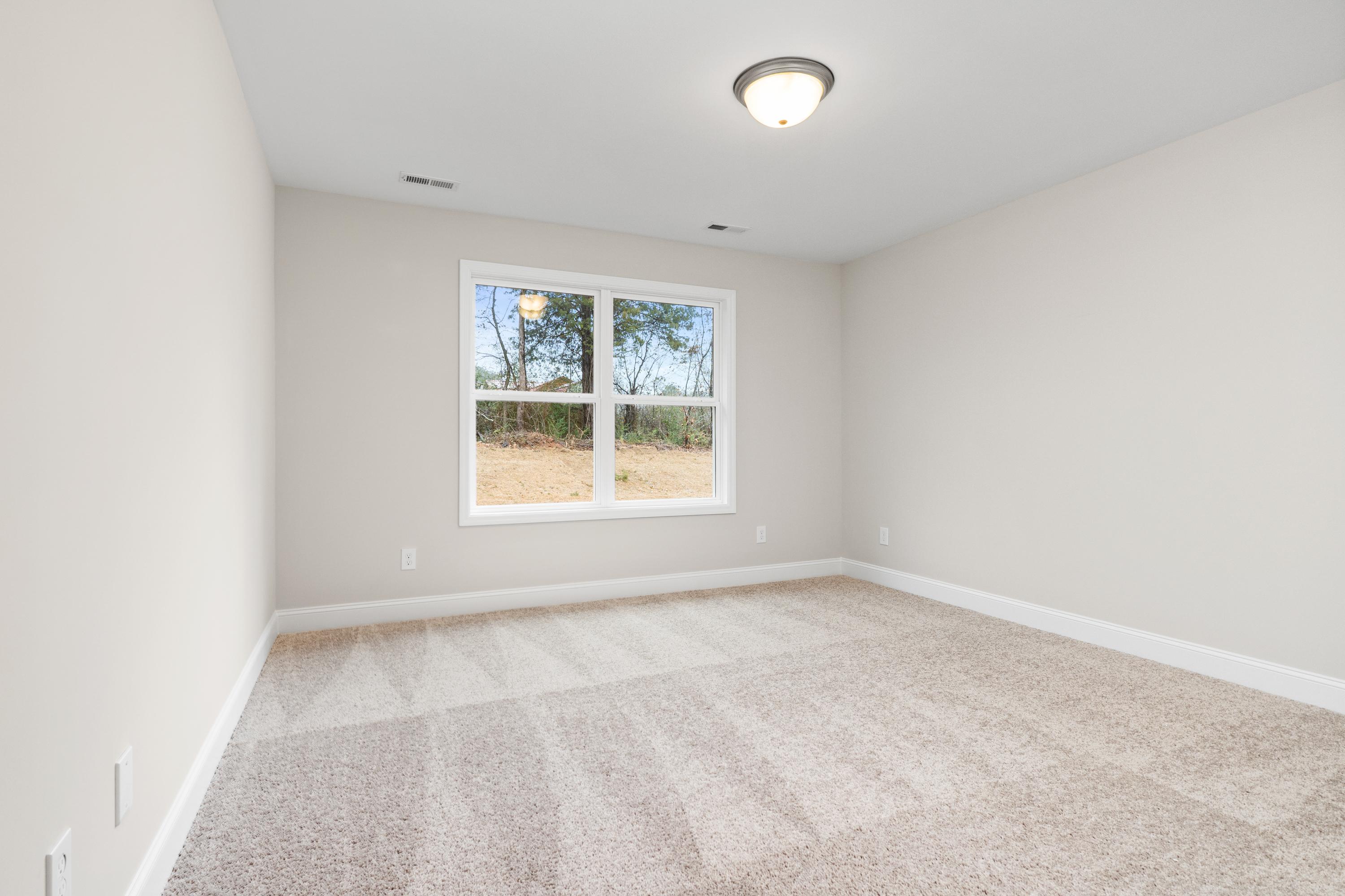 Spacious secondary bedroom in The Asheville home plan with neutral gray walls, large double-hung window, and plush carpet flooring