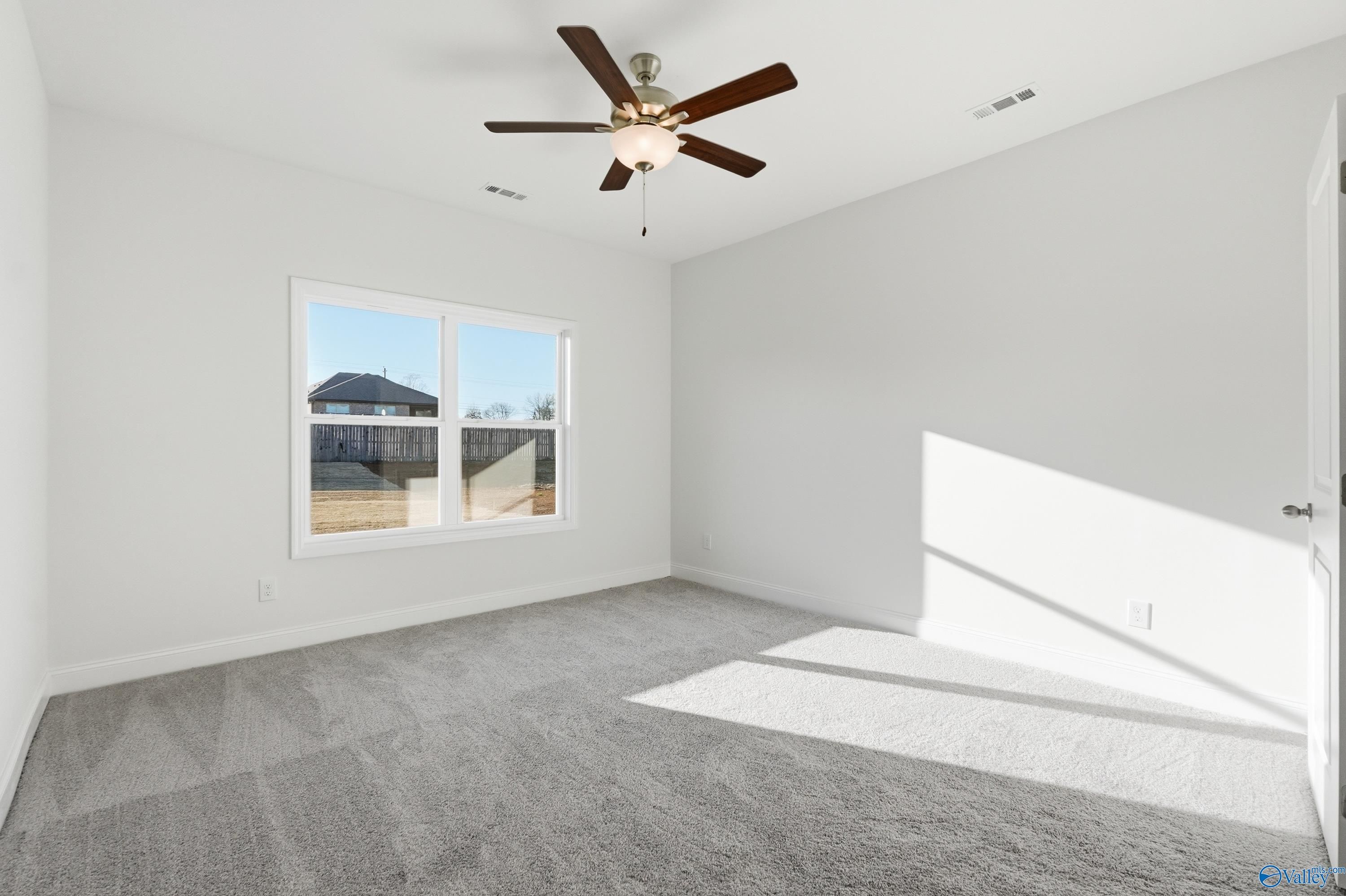 Bright secondary bedroom with white walls, gray carpet, ceiling fan, and large window in Davidson Homes The Asheville C, Meridianville, Alabama
