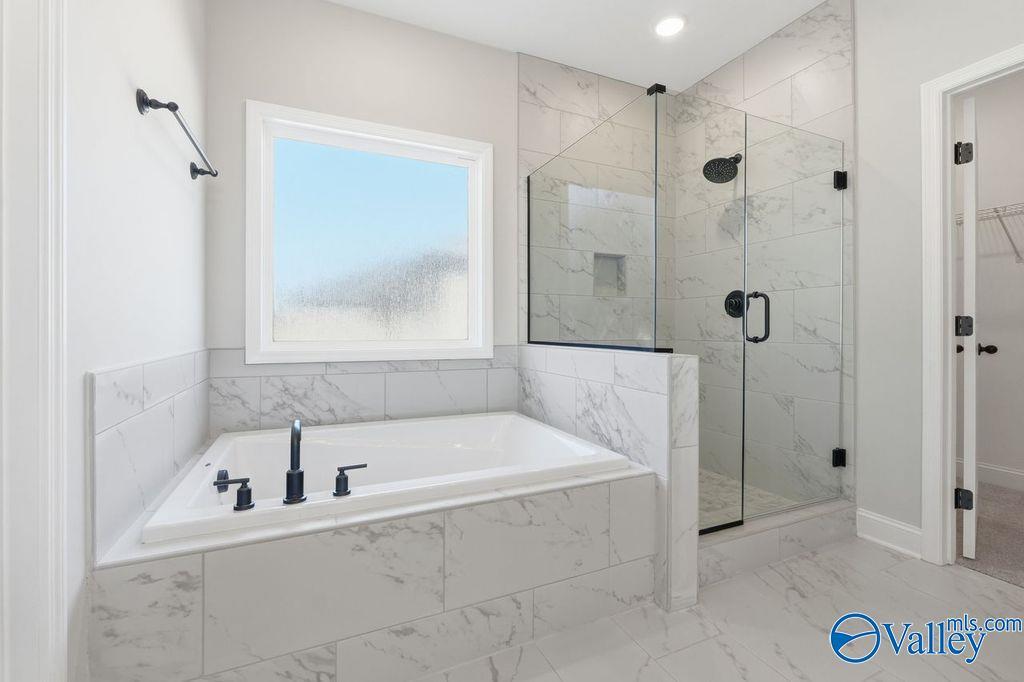 Modern master bathroom with marble-tiled soaking tub and glass-enclosed shower in The Montgomery B, Cain Park, Hartselle.