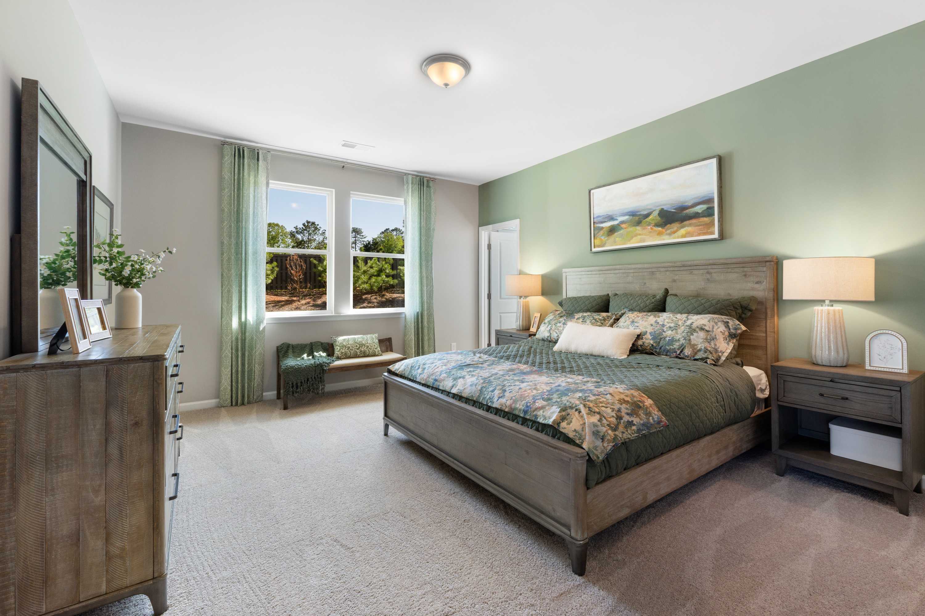 Spacious master bedroom at Evergreen Mill in Madison AL with sage green walls, king bed, floral bedding, and large windows