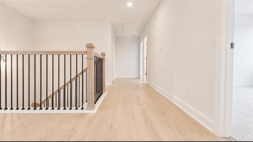Bright second-floor hallway with wood-style flooring and modern iron railing in The Hickory C home at Wehunt Meadows.