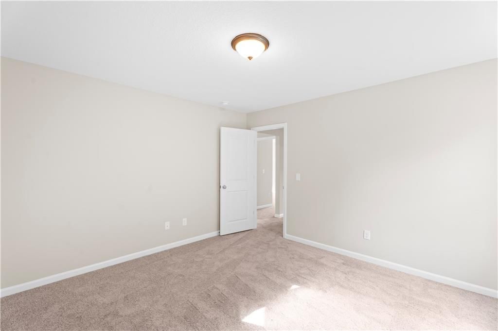 Empty secondary bedroom featuring neutral beige walls, carpeted flooring, open door, and ceiling light in Davidson Homes The Washington, Phenix City, AL