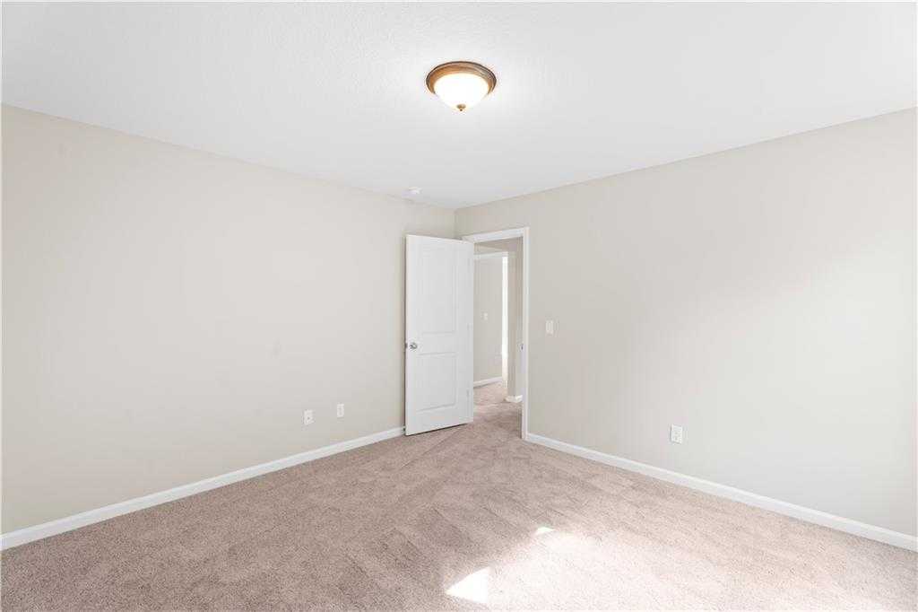 Empty secondary bedroom featuring neutral beige walls, carpeted flooring, open door, and ceiling light in Davidson Homes The Washington, Phenix City, AL