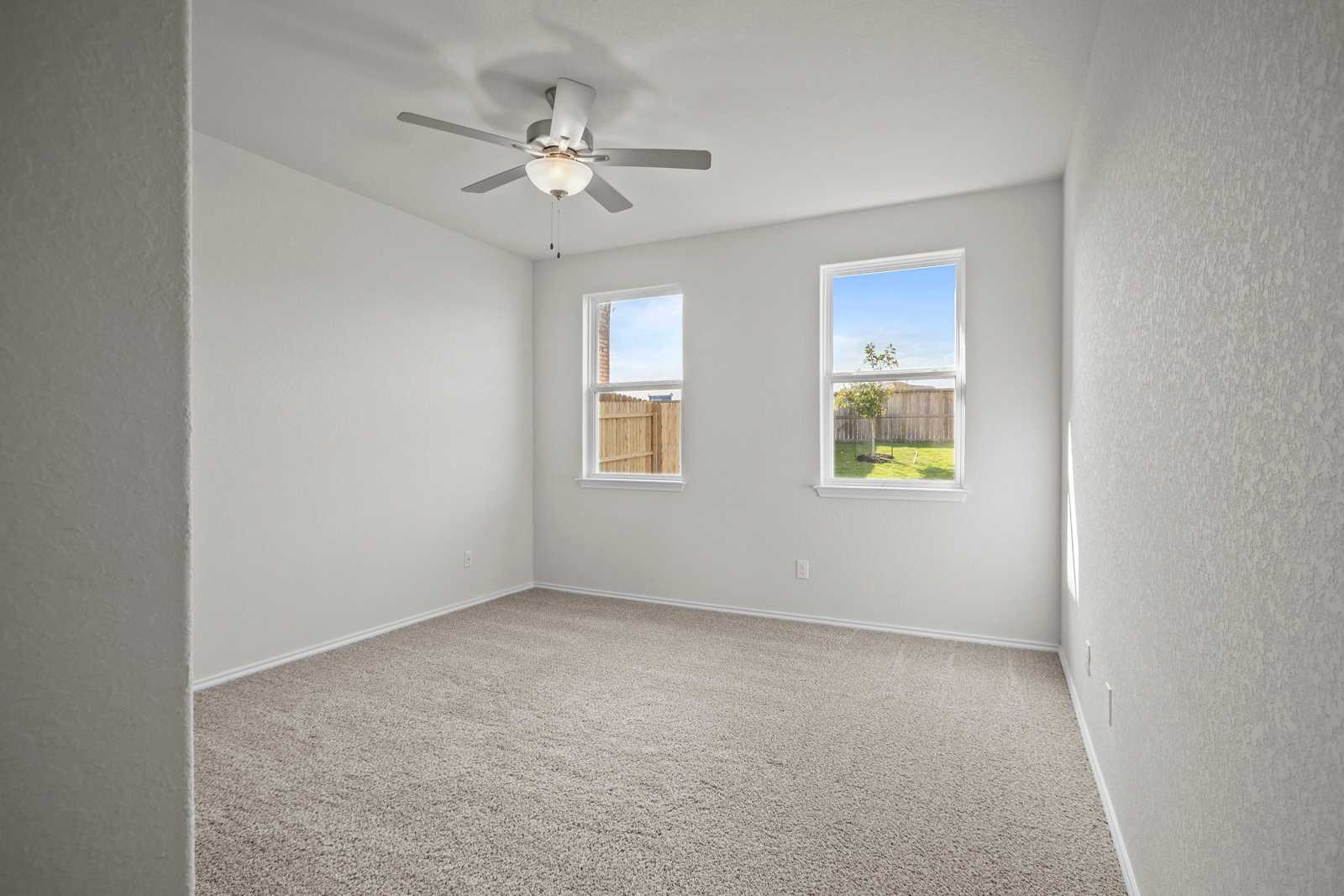 Bright secondary bedroom with ceiling fan, large windows overlooking fenced backyard in Davidson Homes The Redbud B, Josephine, Texas