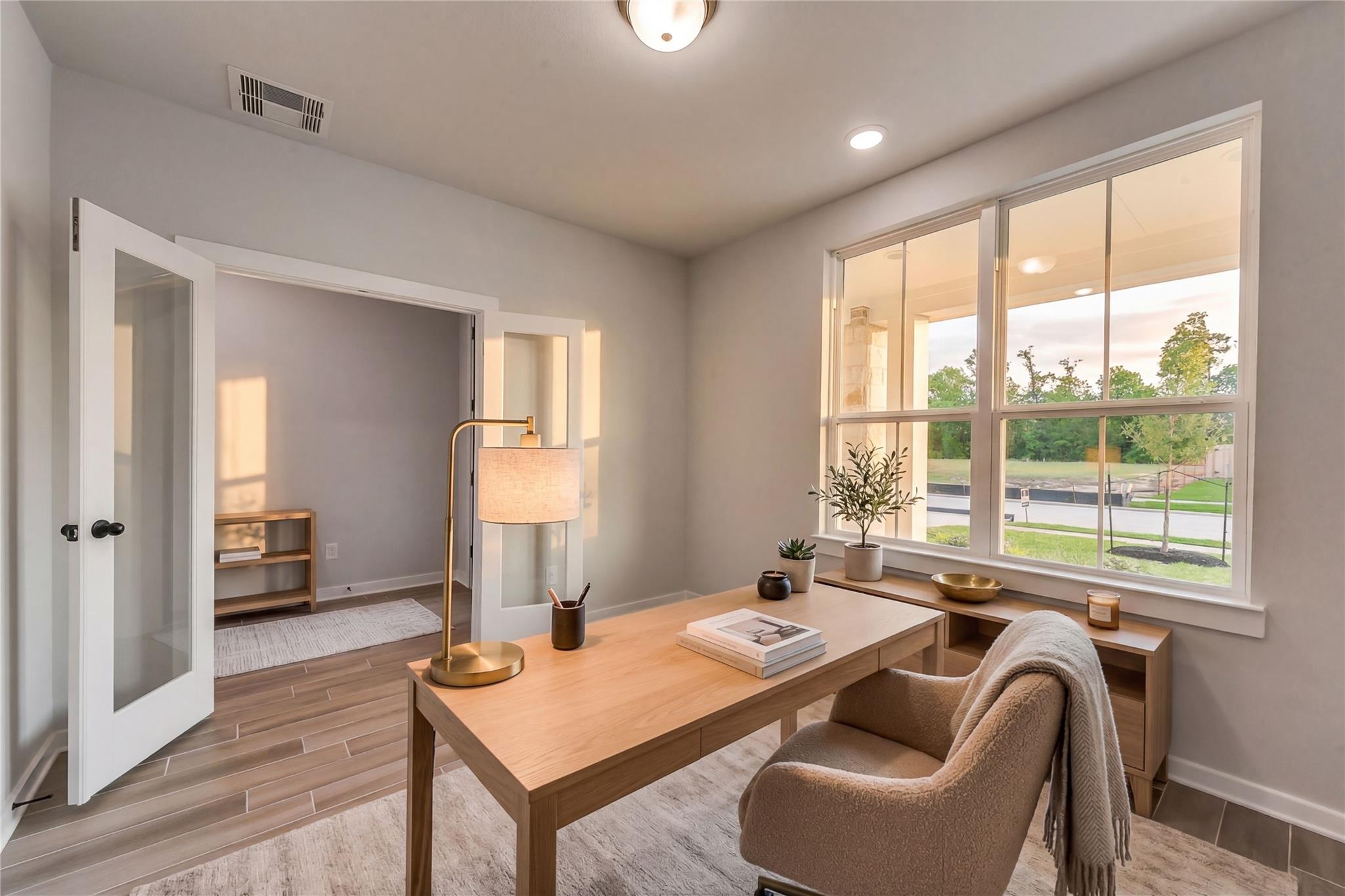 Elegant home office with oak desk, beige armchair, gold lamp, and large windows overlooking green yard in Davidson Homes Sequoia C, Crosby Texas