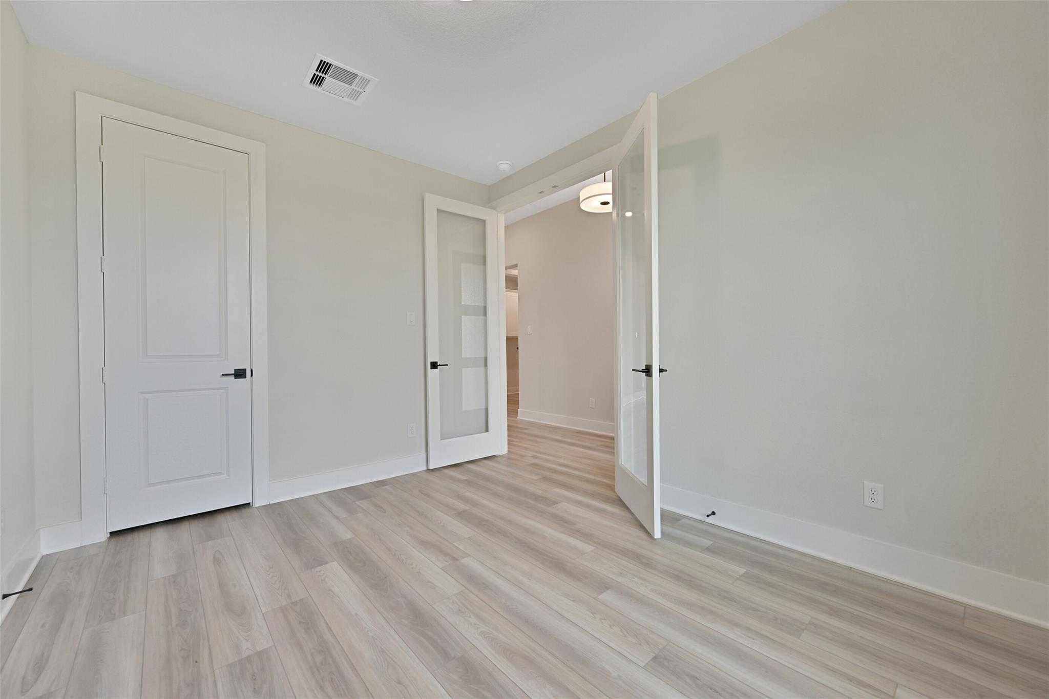 Master bedroom with open doors to adjacent bathroom, beige walls, luxury vinyl plank flooring in Davidson Homes The Edward C, Lago Mar, Texas City
