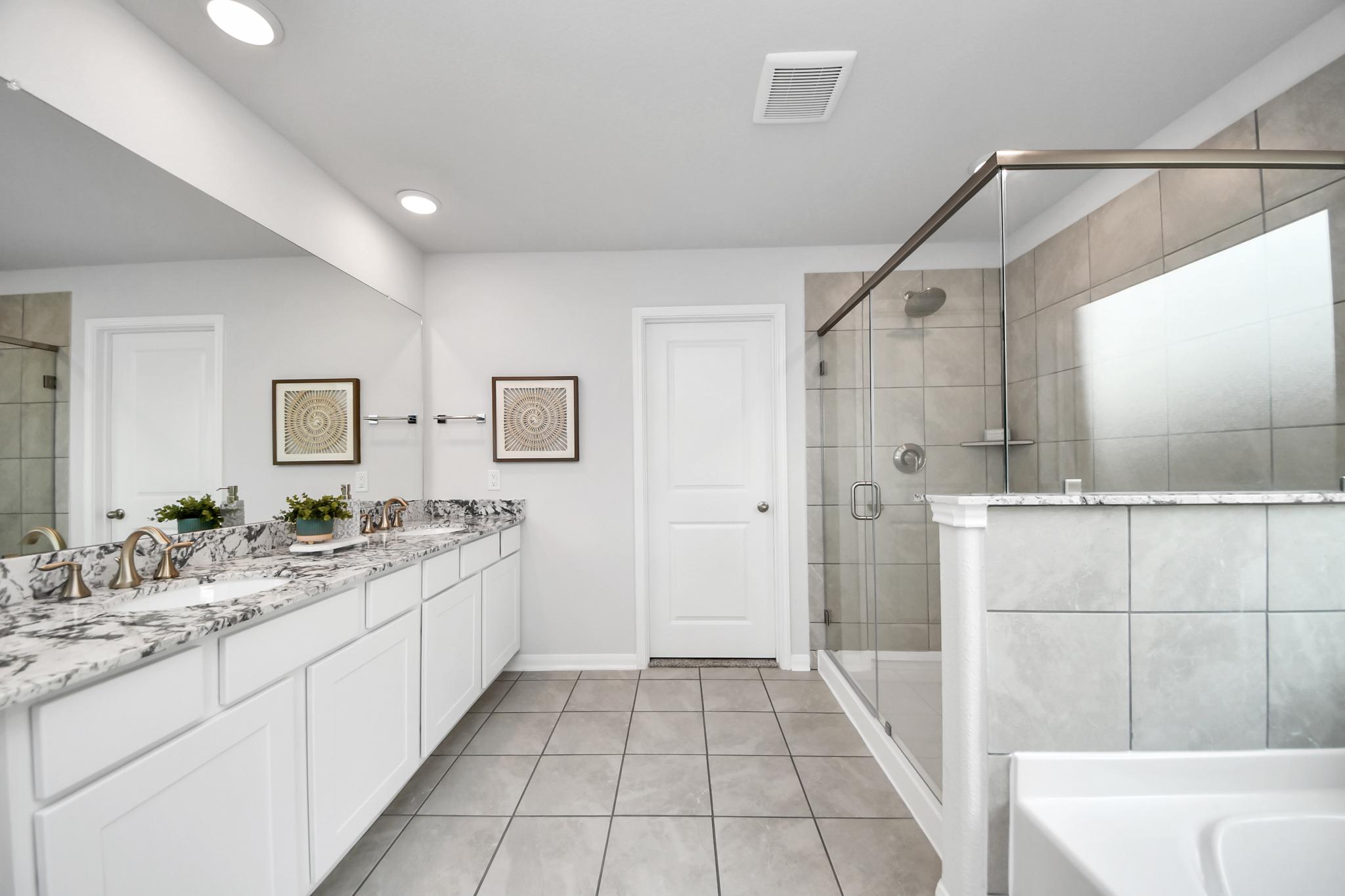 Modern primary bathroom at Sunterra in Katy, TX by Davidson Homes featuring granite countertops and walk-in glass shower.