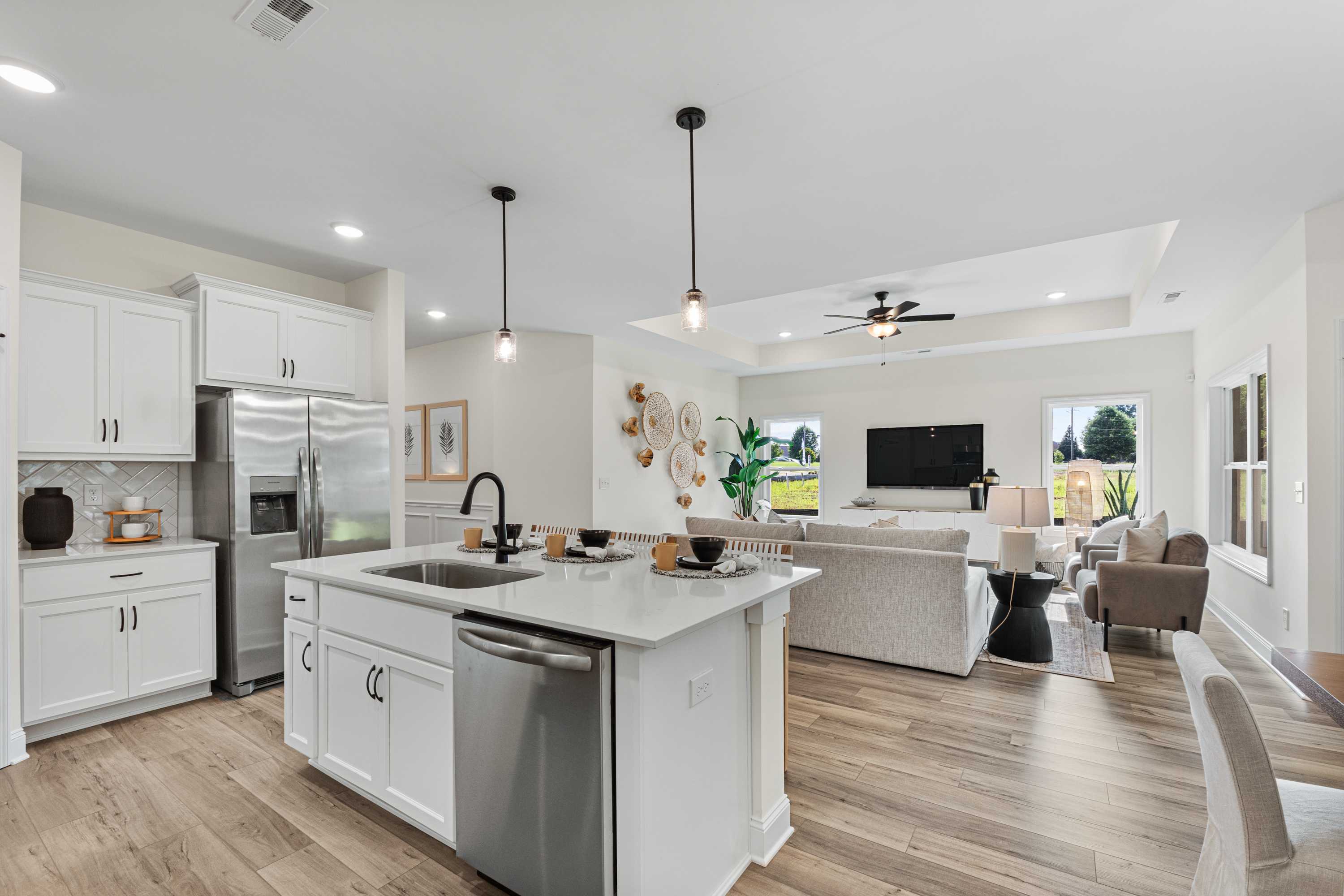 Open-concept kitchen and living room in Lynn Meadows, Meridianville AL with white cabinets, central island, hardwood floors