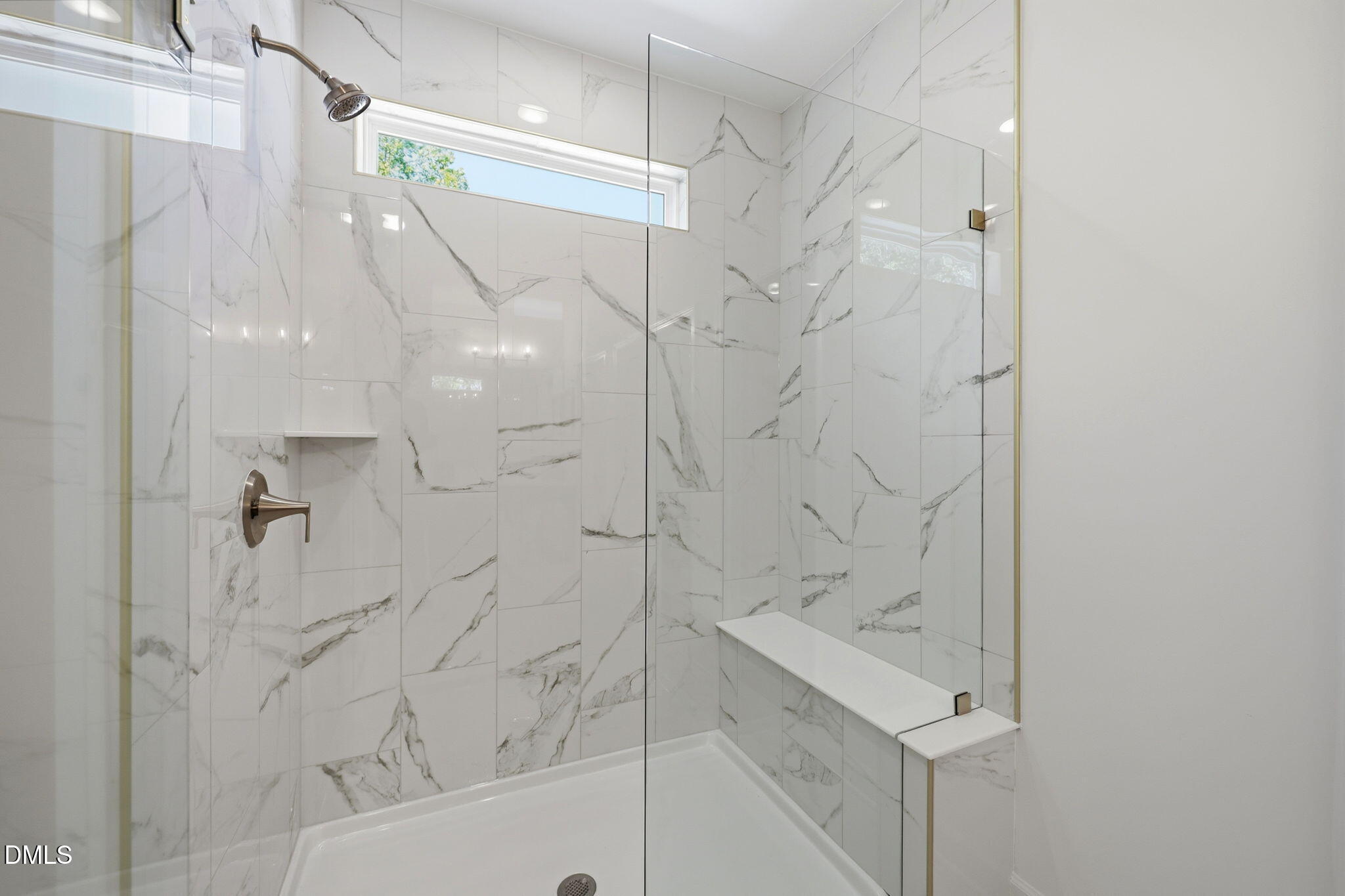 Walk-in shower with marble-look tile, glass door, and built-in bench in The Aspen B floor plan at Wendell Ridge, NC.