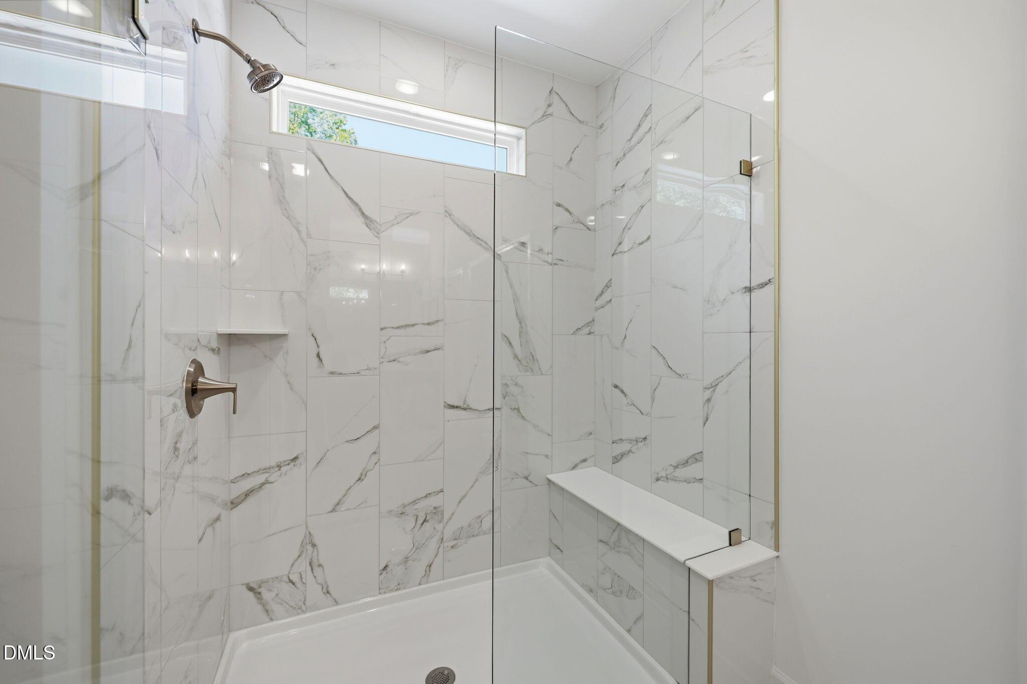 Walk-in shower with marble-look tile, glass door, and built-in bench in The Aspen B floor plan at Wendell Ridge, NC.