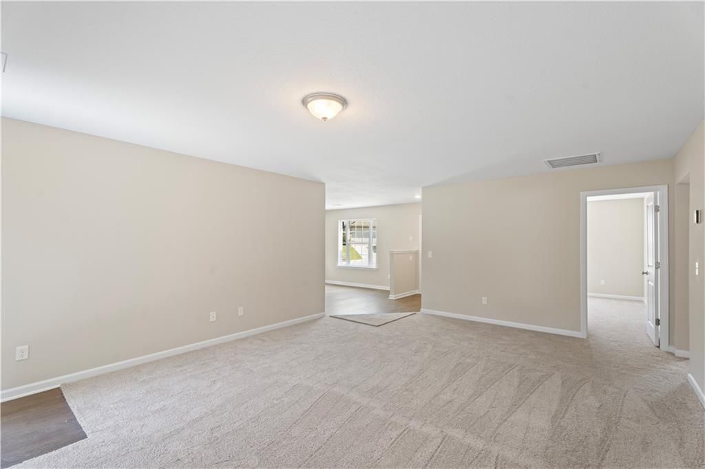 Spacious open living room with beige walls, carpet flooring, and adjacent doorways in The Washington 3-bedroom home, Phenix City, Alabama