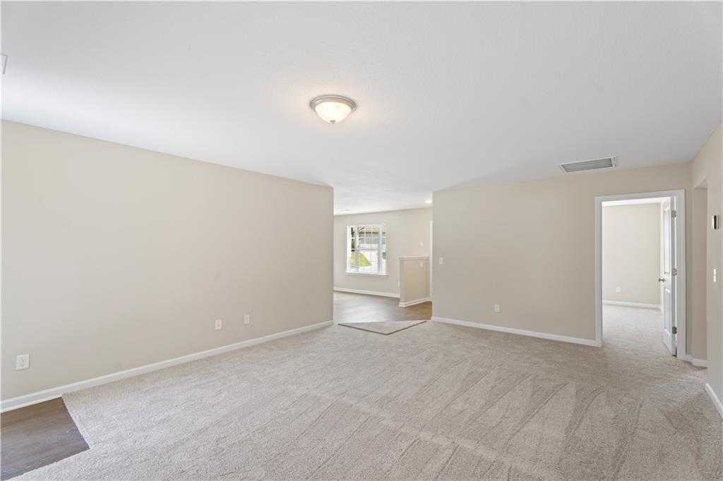 Spacious open living room with beige walls, carpet flooring, and adjacent doorways in The Washington 3-bedroom home, Phenix City, Alabama