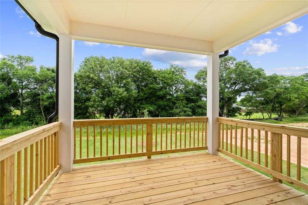 Covered wooden deck with white columns and railings overlooking lush green lawn and trees in Davidson Homes The Hickory B at Wehunt Meadows, Hoschton
