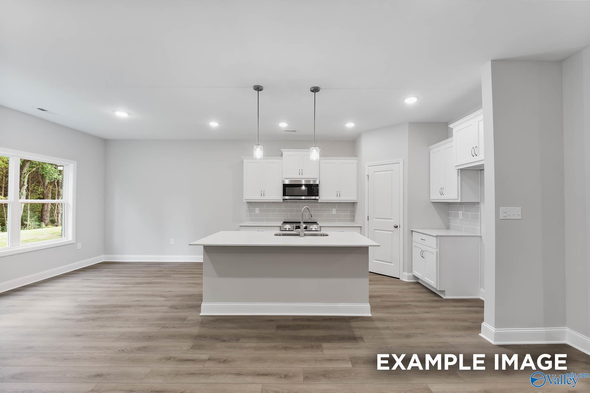 Modern white kitchen island with stainless cooktop, subway tile backsplash, pendant lights in The Asheville C, Athens AL