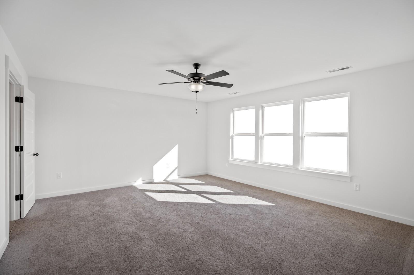 Bright empty bedroom with three large windows, ceiling fan, and carpeted floor in Davidson Homes The Willow C, Gallatin, TN
