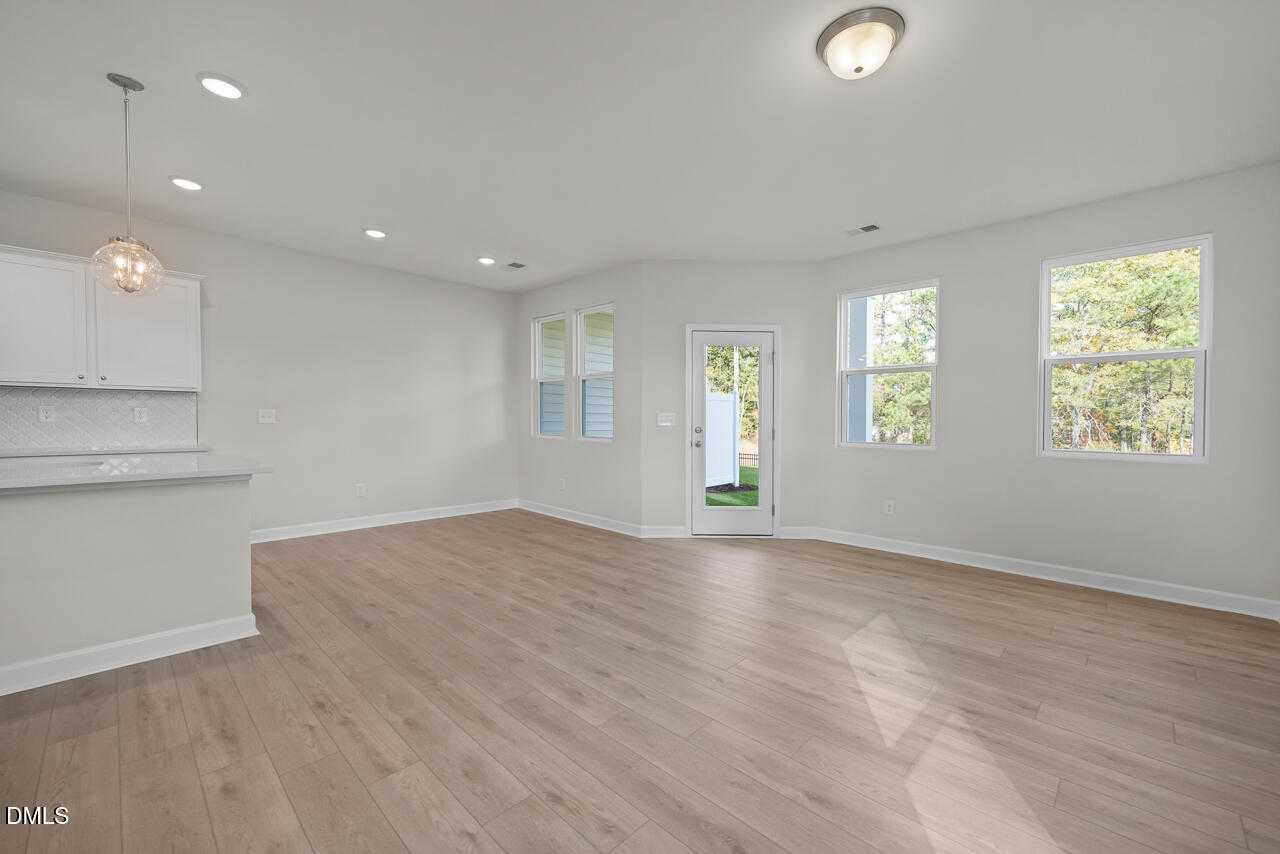 Bright open-concept living-kitchen with white cabinets, pendant lights, and large windows in The Graham Exterior, Fuquay-Varina, NC