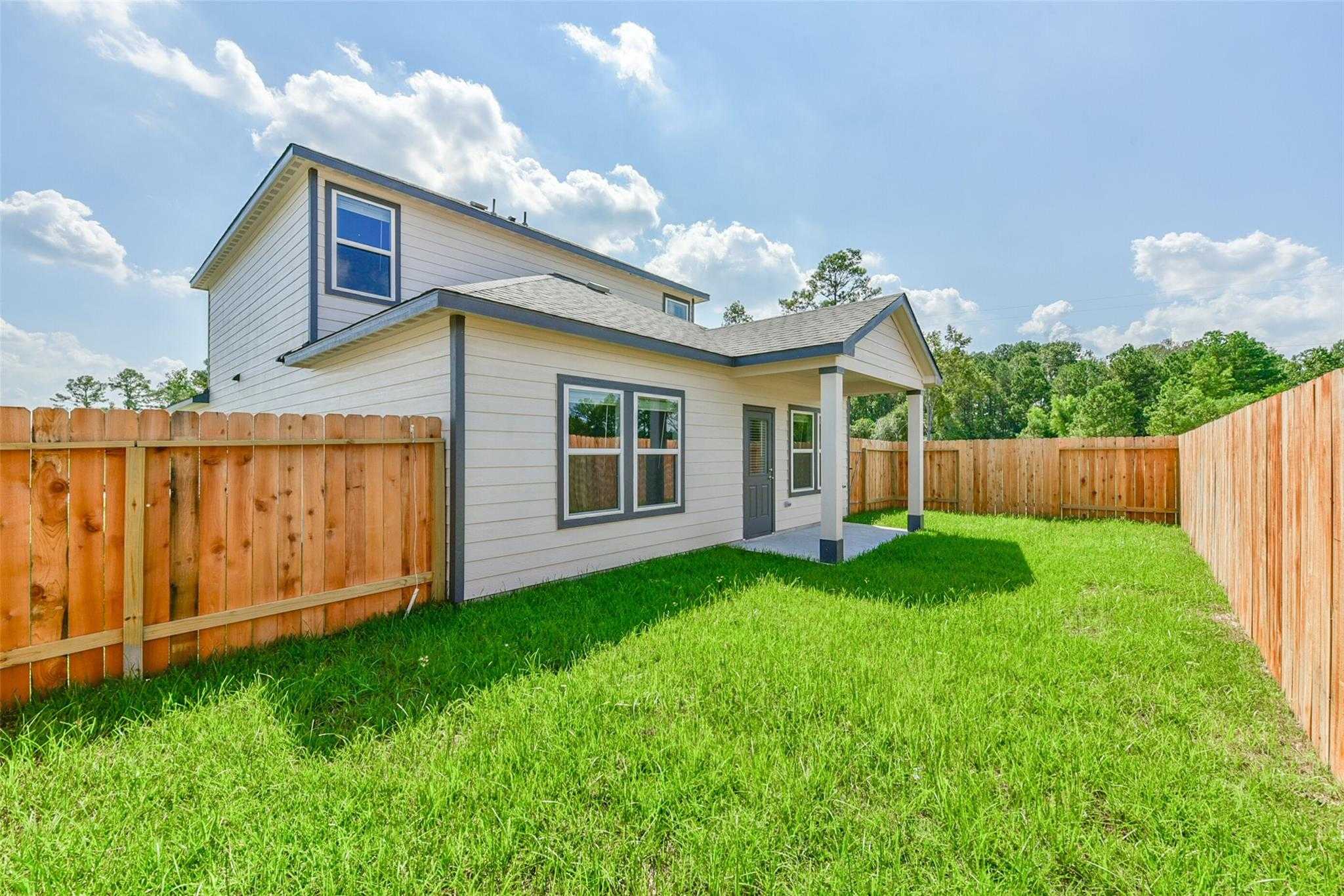 Two-story Sabine E home exterior with covered porch, fenced backyard, and lush green lawn in Dayton, Texas