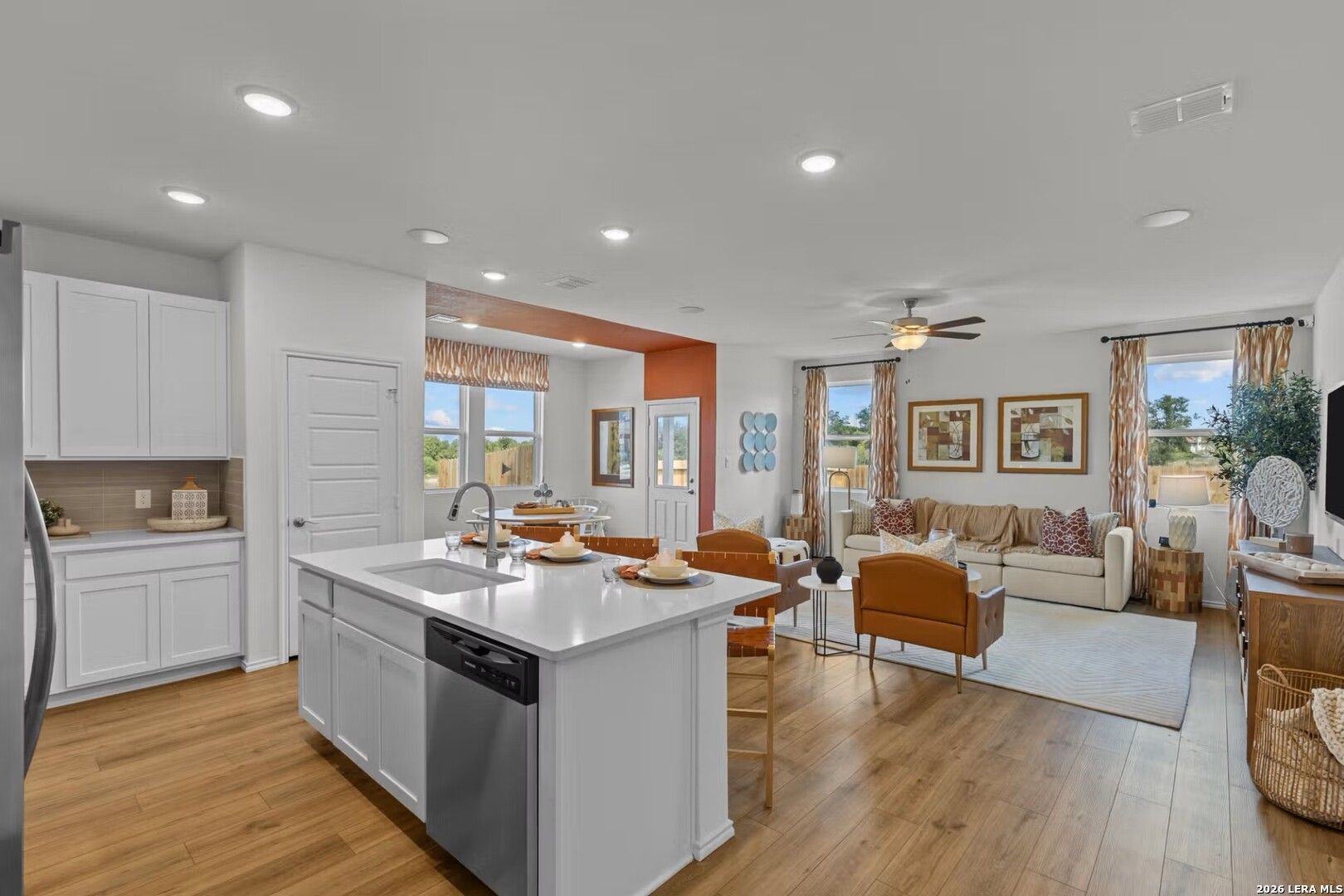 Open-concept kitchen with white island, stainless dishwasher, and adjacent living room in The Daphne K, Bricewood, San Antonio