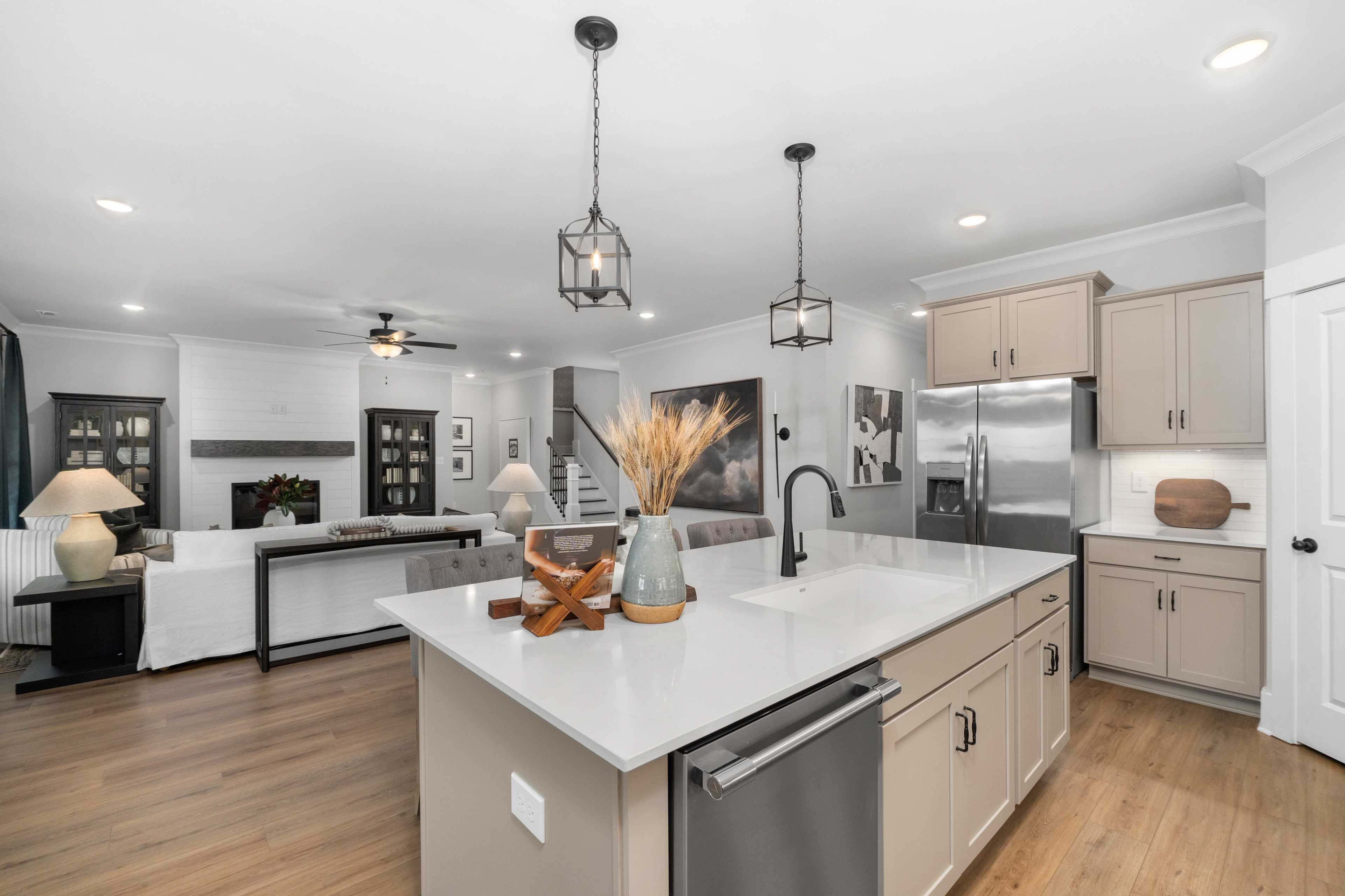 Open-concept kitchen and living room at Kendall Farms in Toney, Alabama featuring white quartz island, beige cabinets, hardwood floors, and fireplace