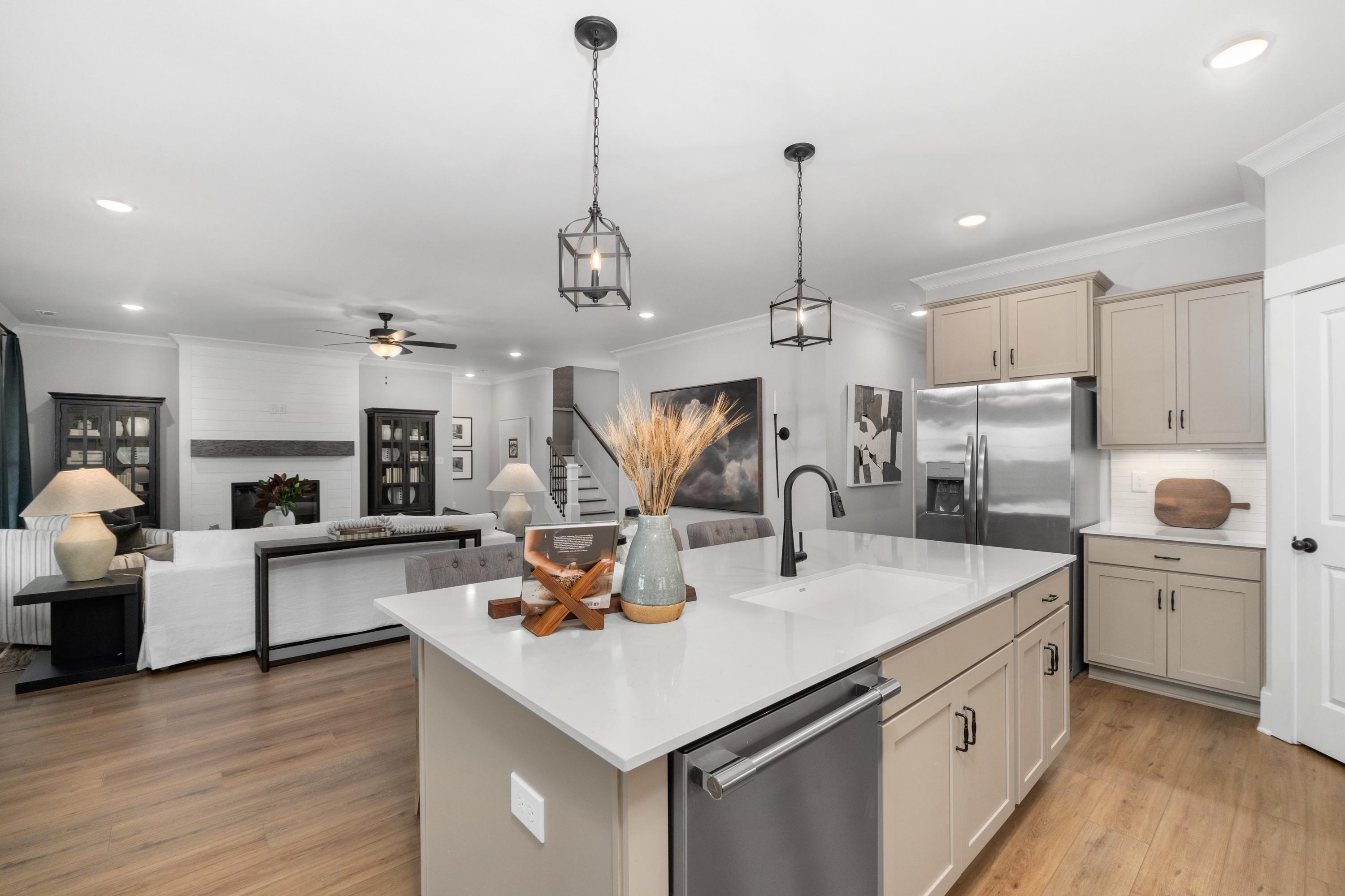 Open-concept kitchen and living room at Kendall Farms in Toney, Alabama featuring white quartz island, beige cabinets, hardwood floors, and fireplace