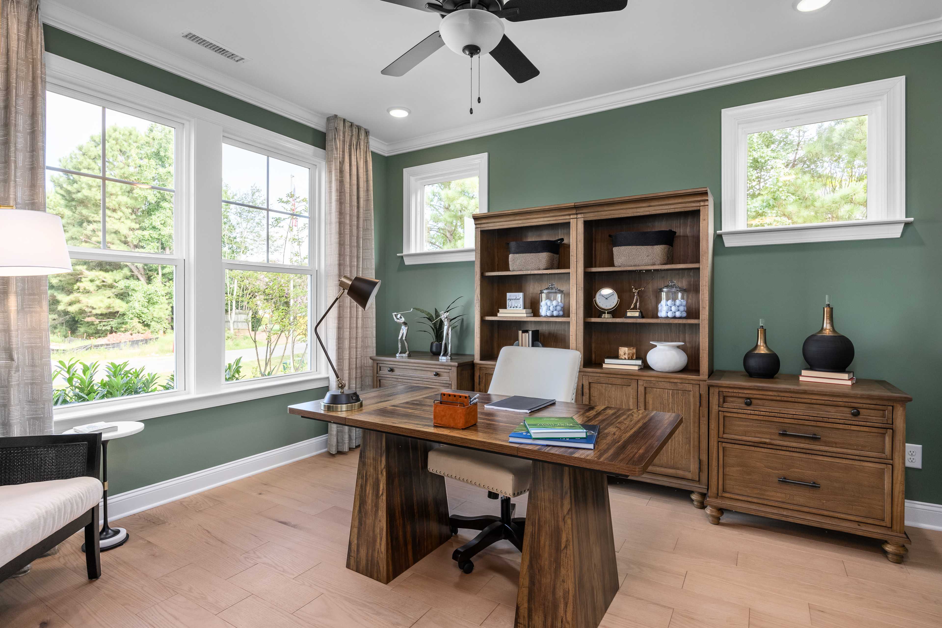 Modern home office at Laneridge Estates in Raleigh NC with sage green walls, wooden desk, bookshelves, and large windows