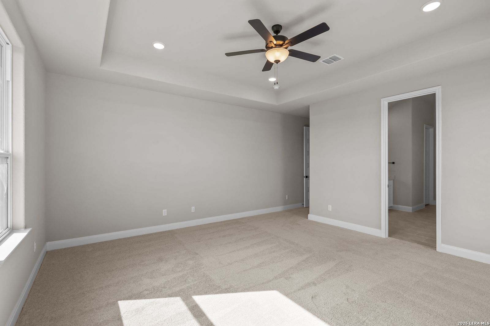 Spacious primary bedroom with tray ceiling, ceiling fan, and carpet in Davidson Homes The Foster E, Potranco Oaks, Castroville, Texas