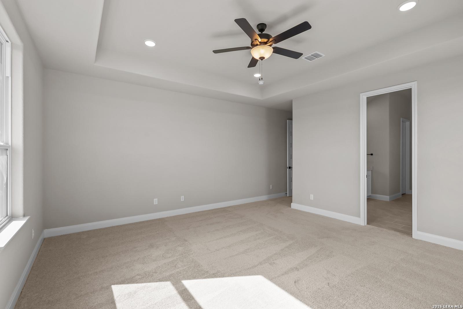 Spacious primary bedroom with tray ceiling, ceiling fan, and carpet in Davidson Homes The Foster E, Potranco Oaks, Castroville, Texas