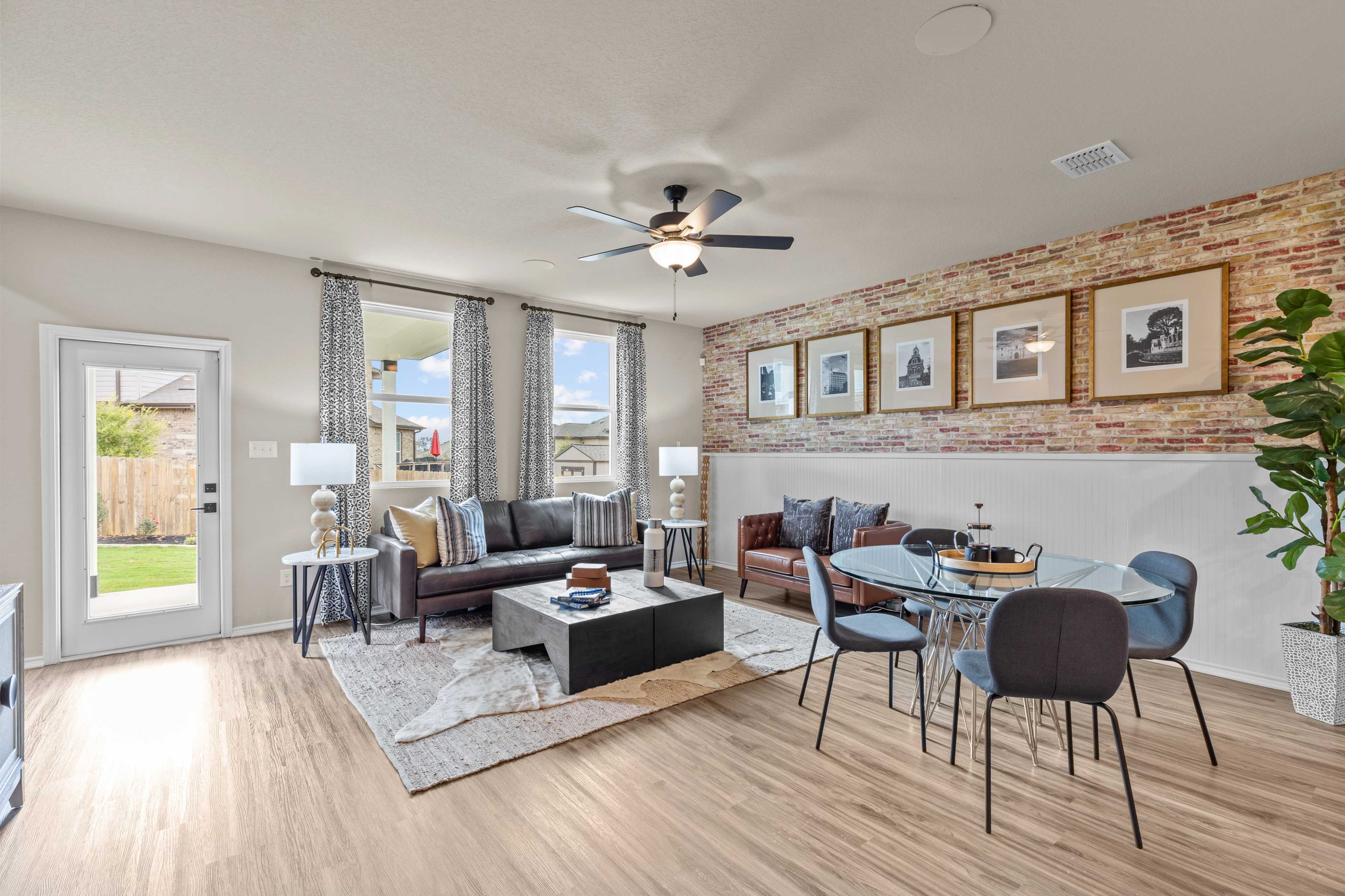 Open-concept living room in Morgan Meadows, San Antonio TX by Davidson Homes featuring brick accent wall, leather sofas, and hardwood floors