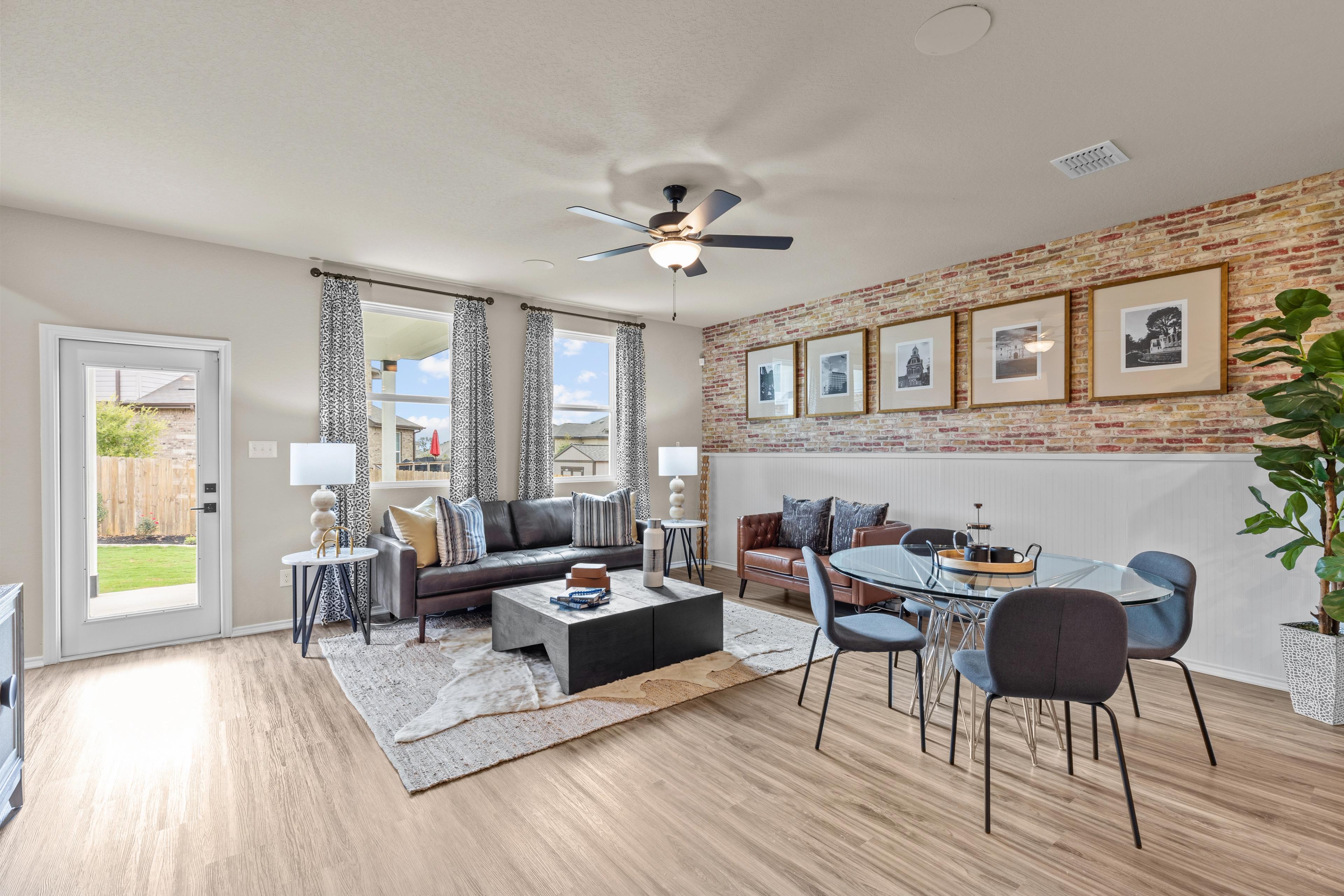 Open-concept living room in Morgan Meadows, San Antonio TX by Davidson Homes featuring brick accent wall, leather sofas, and hardwood floors