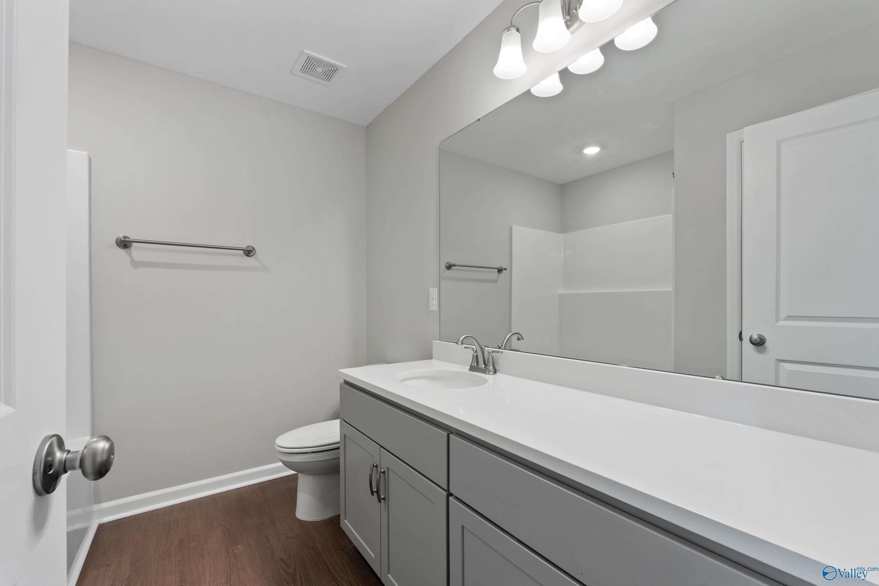 Modern gray bathroom with white vanity, single sink, large mirror, toilet, and walk-in shower in Davidson Homes The Dorado, Athens AL