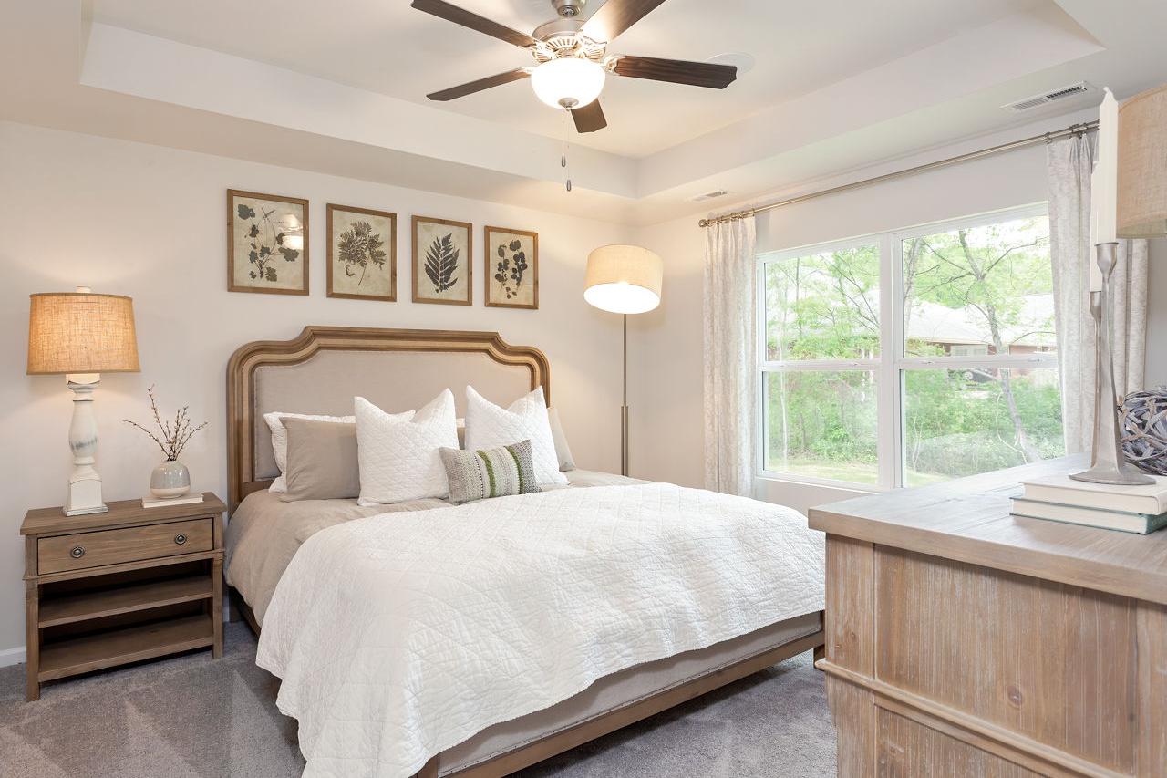 Serene master bedroom in The Franklin C with tufted bed, ceiling fan, botanical art, and large window to greenery